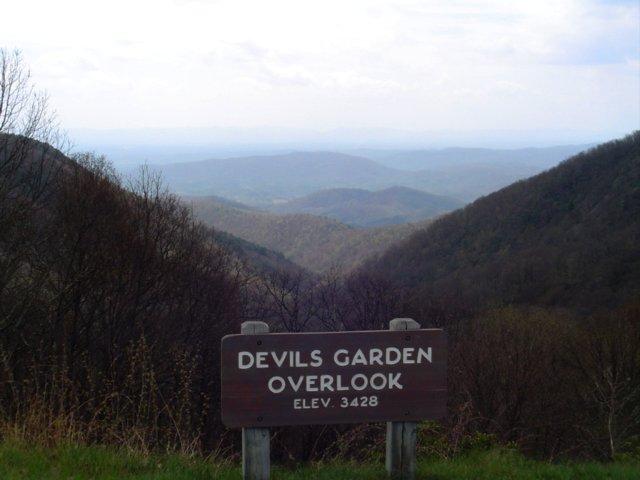 A wooden sign overlooks a vast, hazy mountain range under an overcast sky.