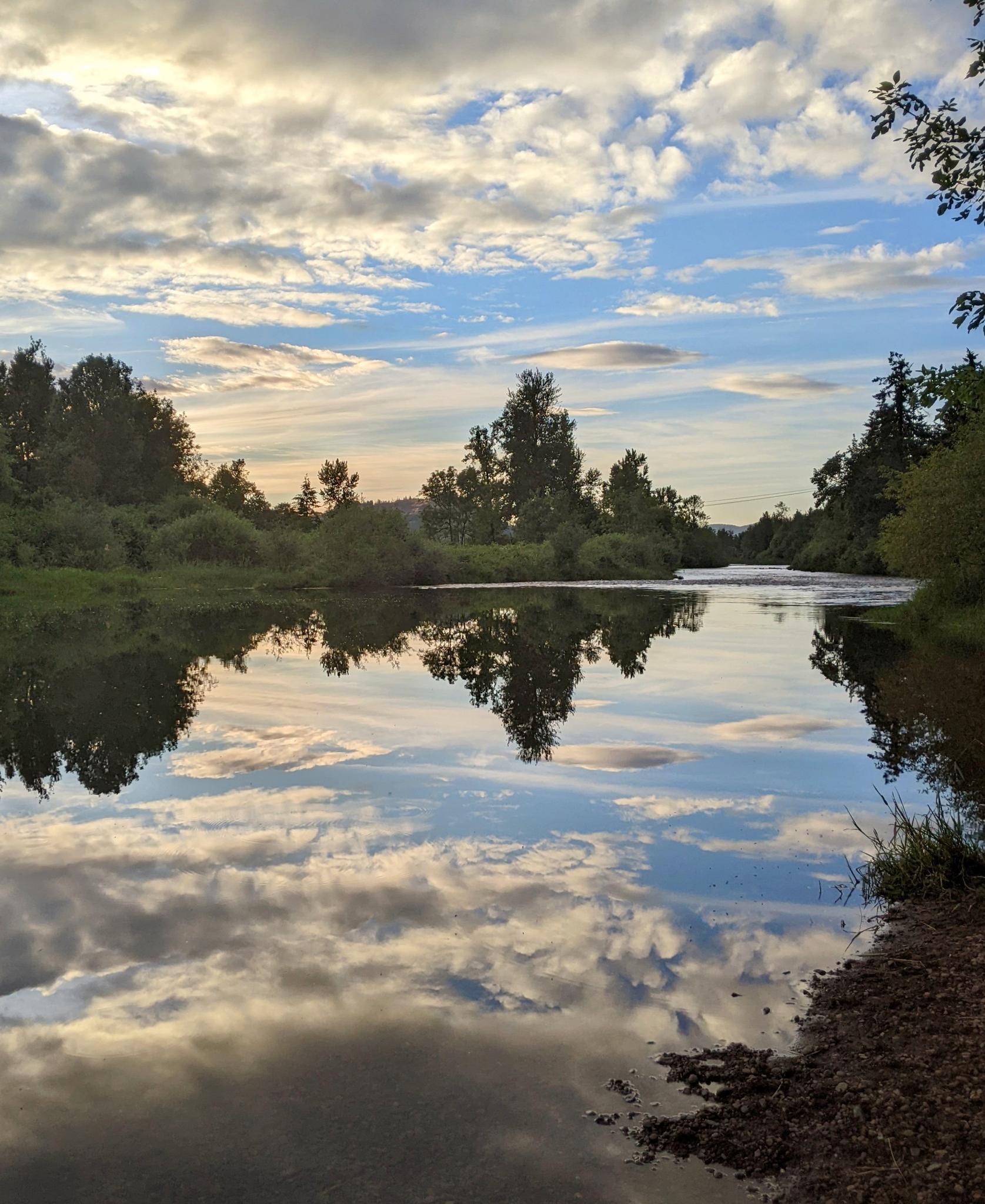 Calm river reflecting a dramatic cloudy sky and surrounding green trees.