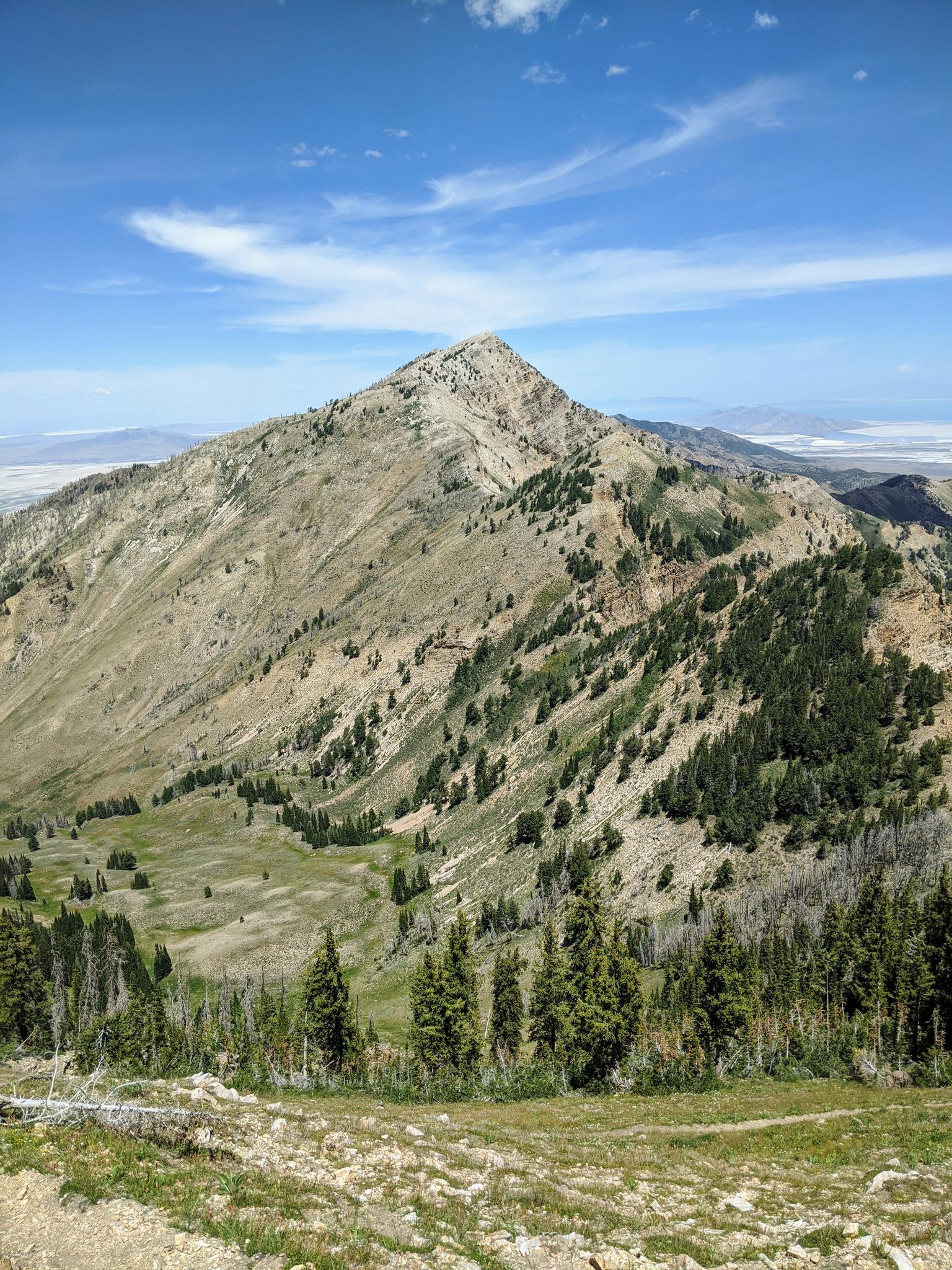 Majestic mountain peak overlooking green valleys and distant plains under a cloudy sky.