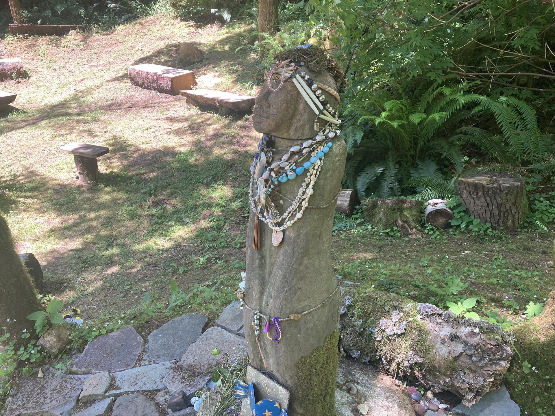 A decorated wooden statue stands in a sunlit forest clearing.