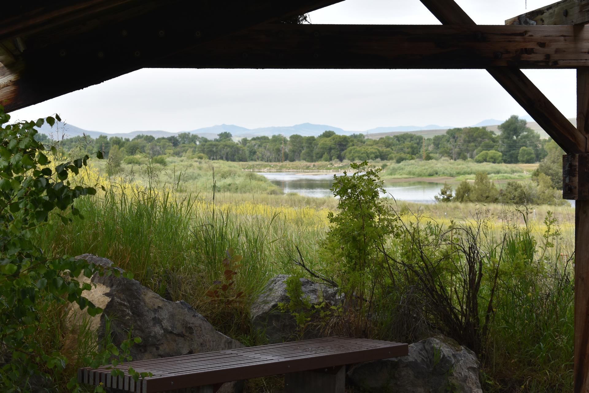 View from a wooden shelter overlooking a wetland with lakes and distant mountains.