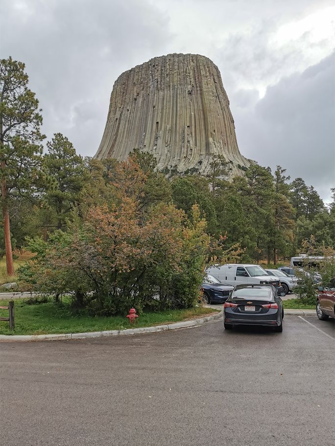 A large, columnar rock formation rises behind a parking lot on an overcast day. - Tower Trail