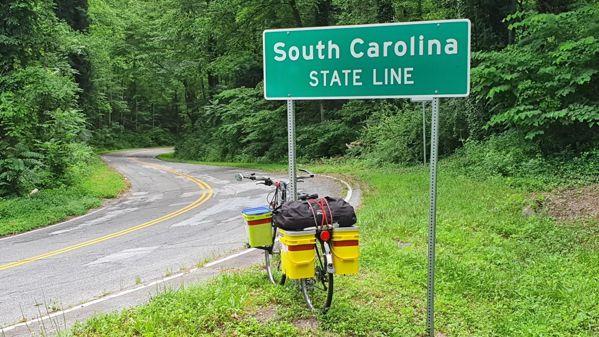 A loaded touring bicycle parked next to a green sign on a winding forest road.