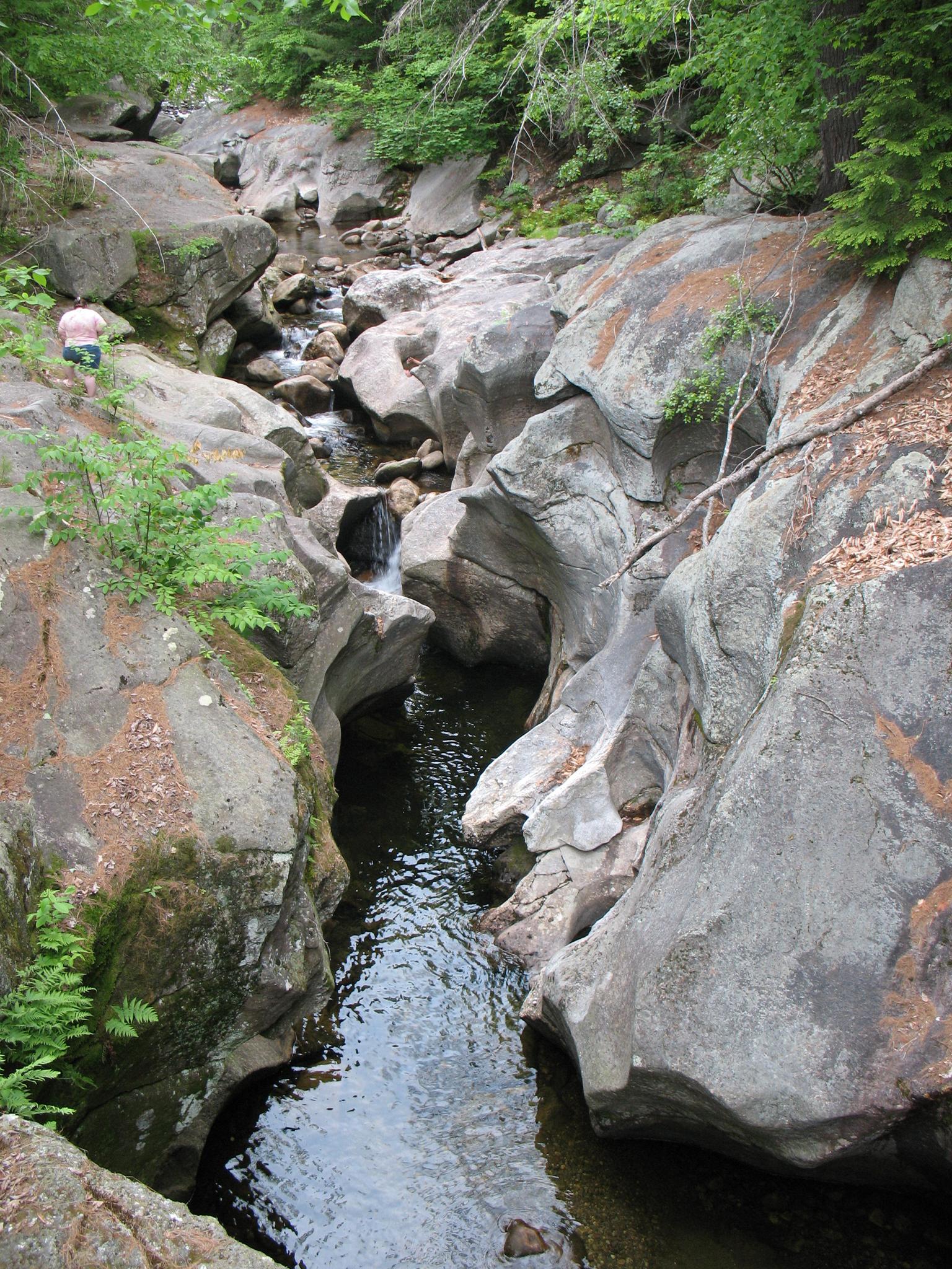 A person stands on rocks overlooking a narrow, rocky gorge with a flowing stream.