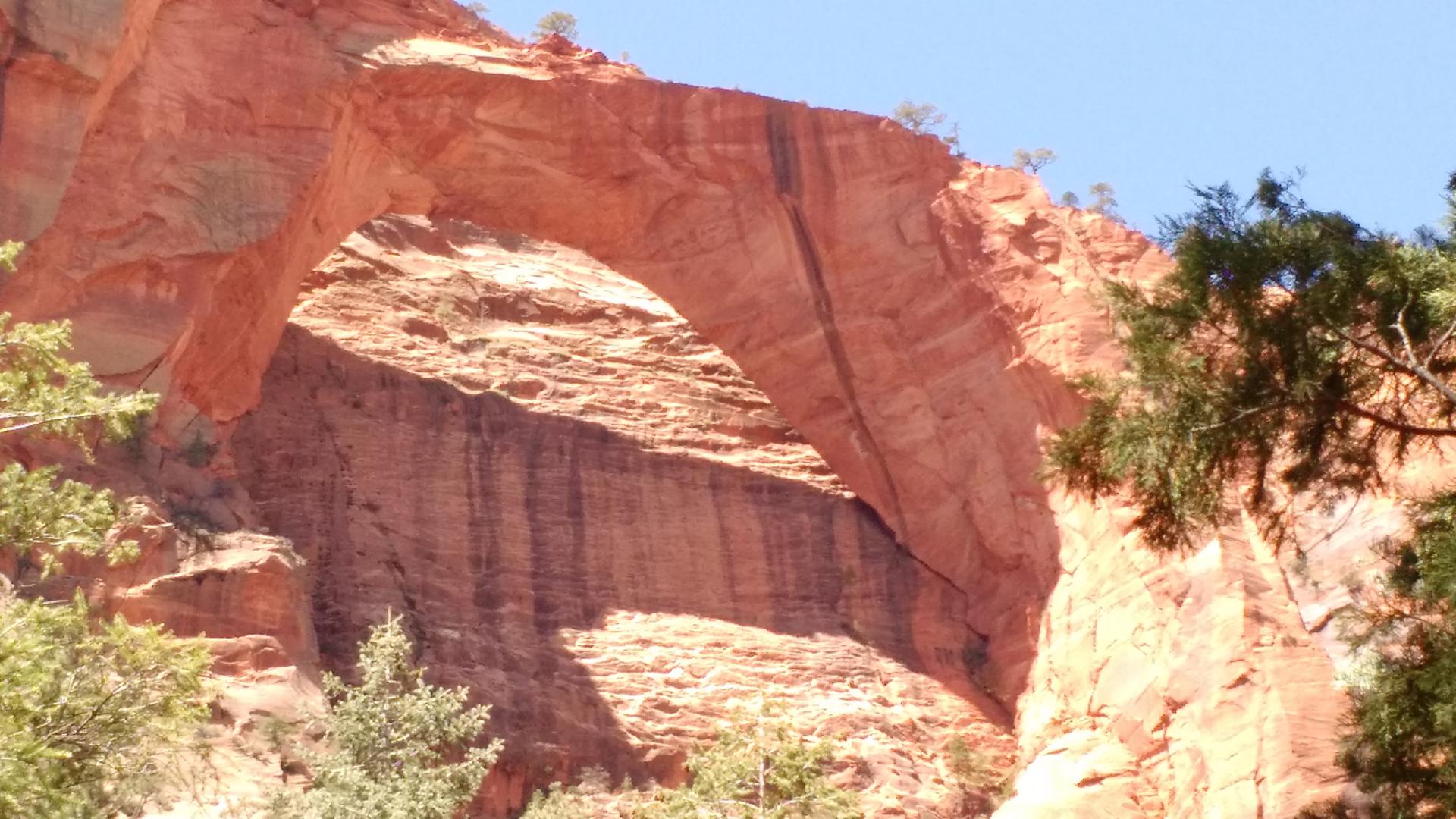 Close-up of a natural red rock arch against a clear blue sky.