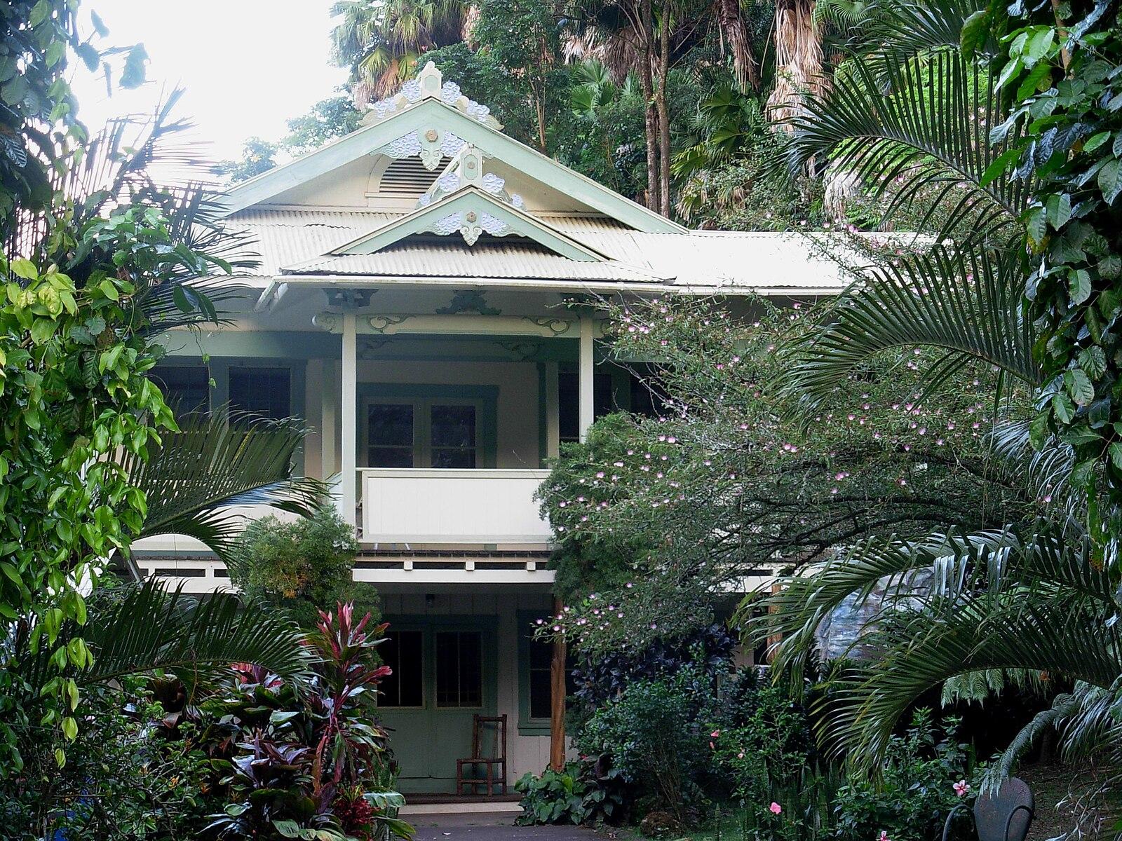 An old house with a porch nestled among dense tropical greenery.
