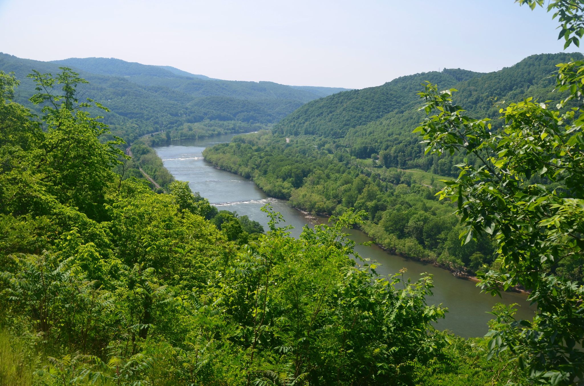 A winding river flows through a lush green mountain valley on a bright day. - Big Branch Trail