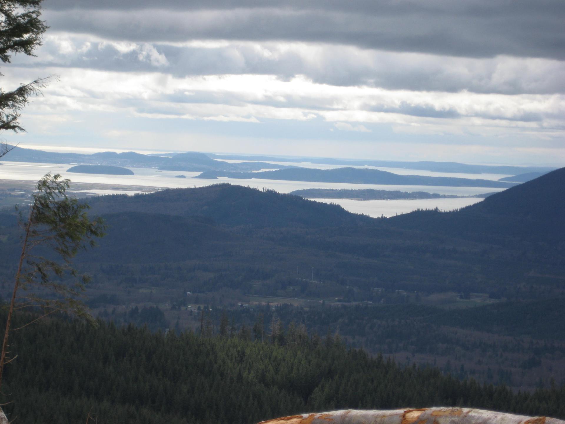 Overcast view of forested hills, islands, and water under a cloudy sky.