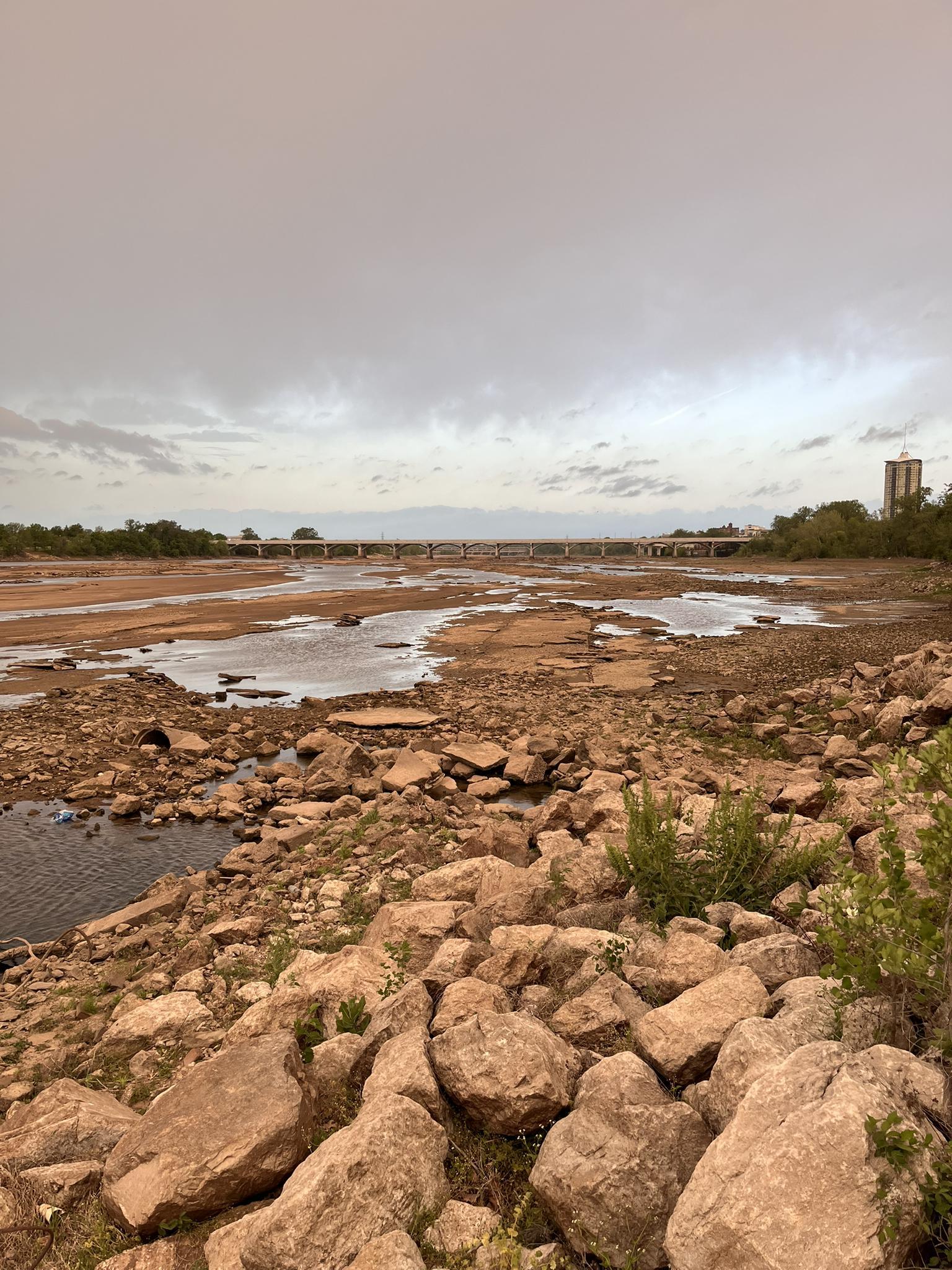 Rocky, dry riverbed with small pools of water under a cloudy sky.