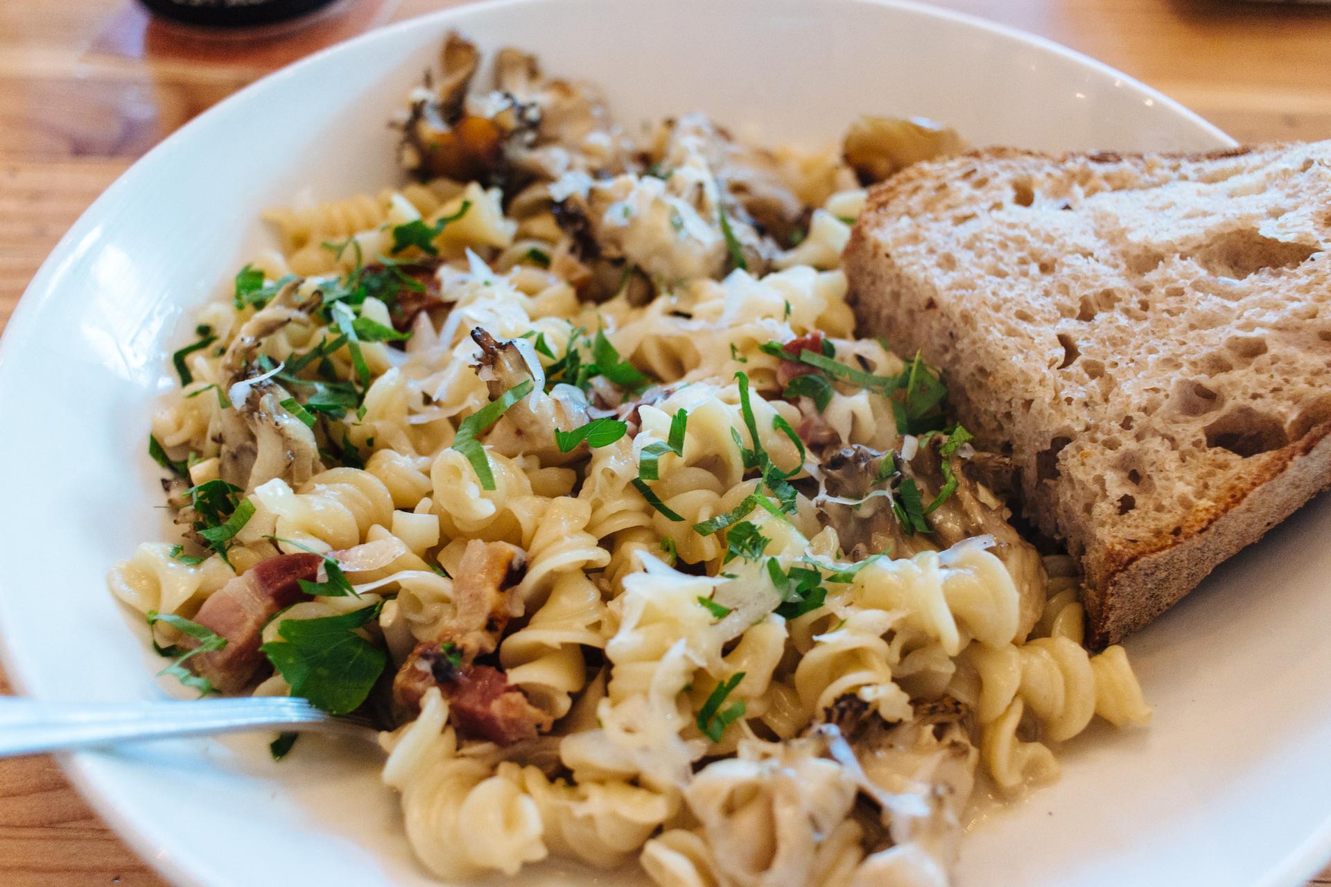 Close-up of a plate of pasta with herbs and a slice of bread.