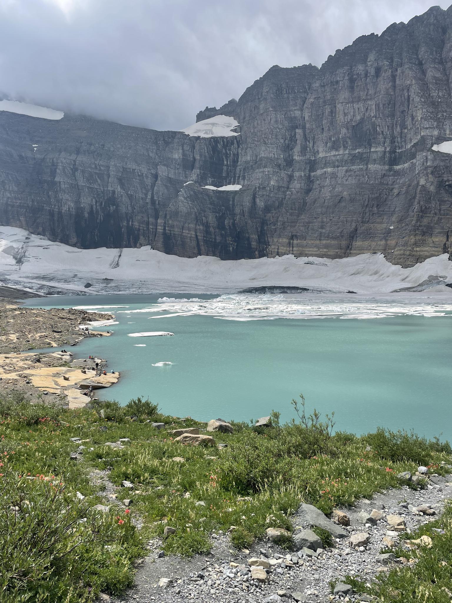 A turquoise lake with ice chunks, backed by a massive rocky mountain face.