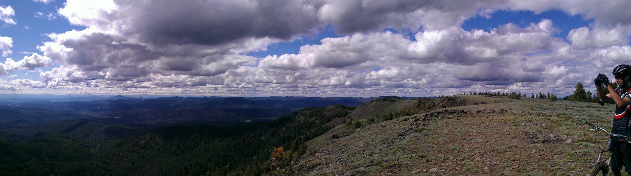 Person with bike on rocky hill overlooking forested valleys under a cloudy sky. - Lookout Mountain and Mother Lode Mine Loop