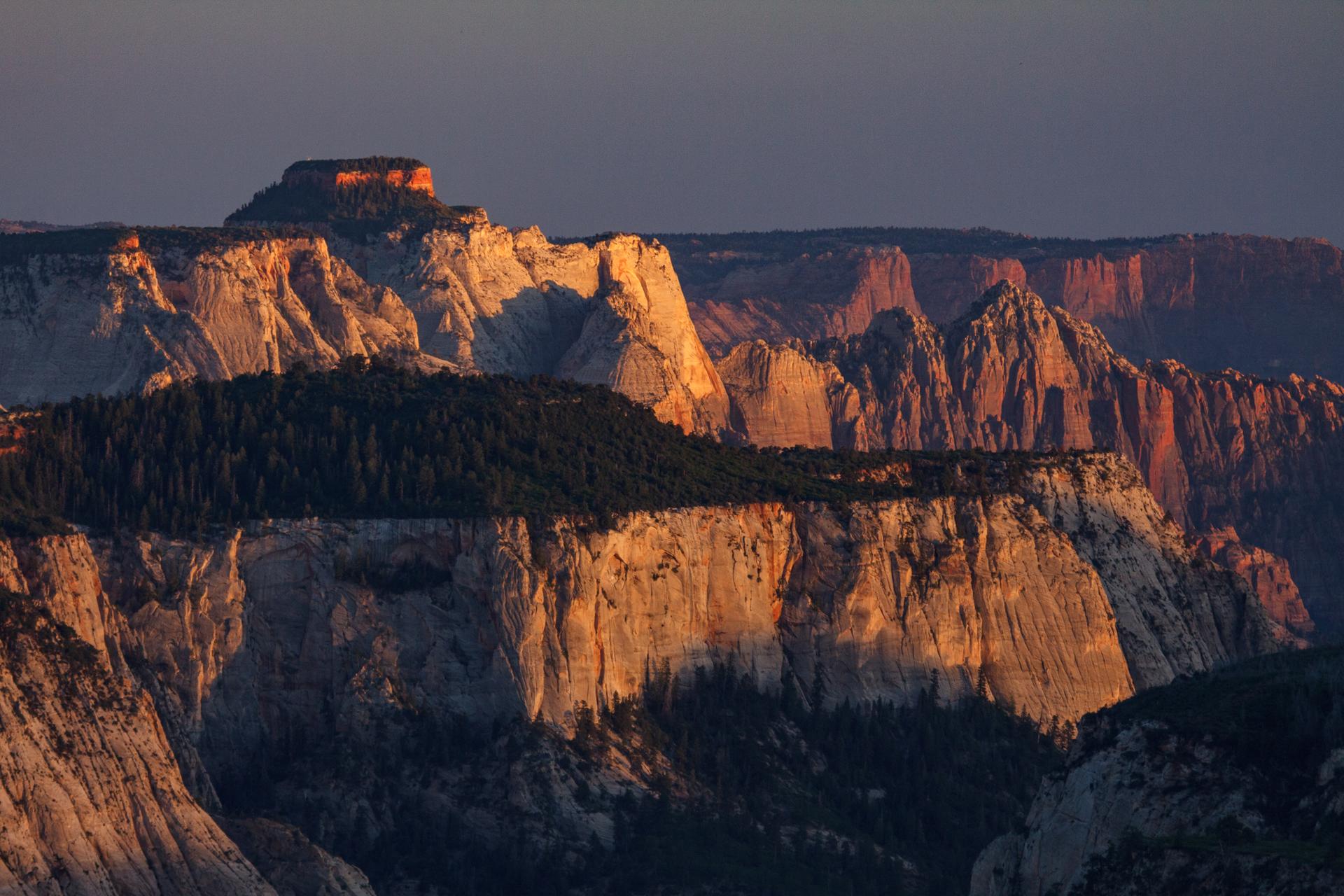 Dramatic desert cliffs and canyons bathed in golden sunset light.
