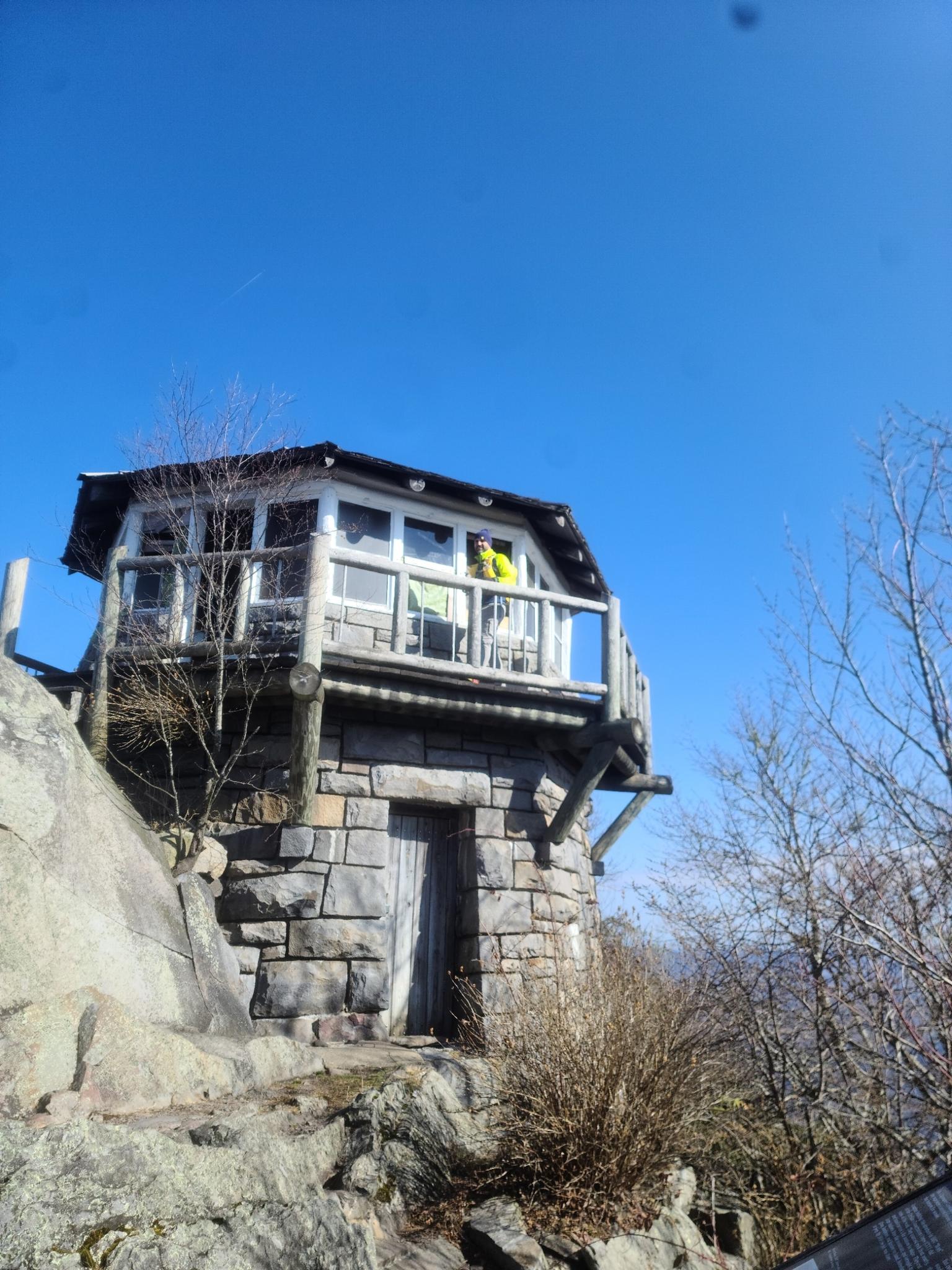 Stone and wood lookout tower on a rocky peak, person on balcony.