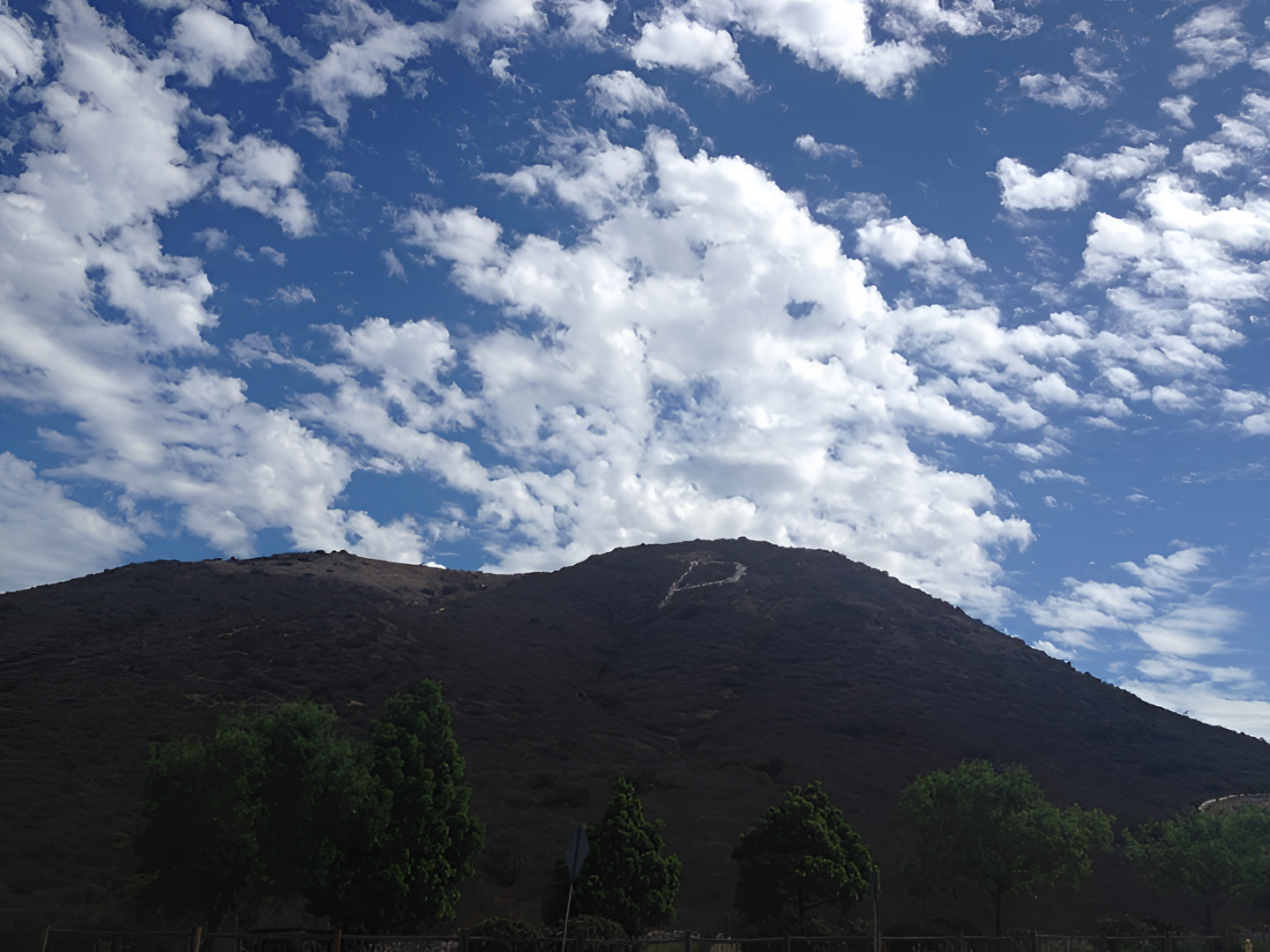 A large, shadowed hill with a white "P" under a cloudy blue sky.