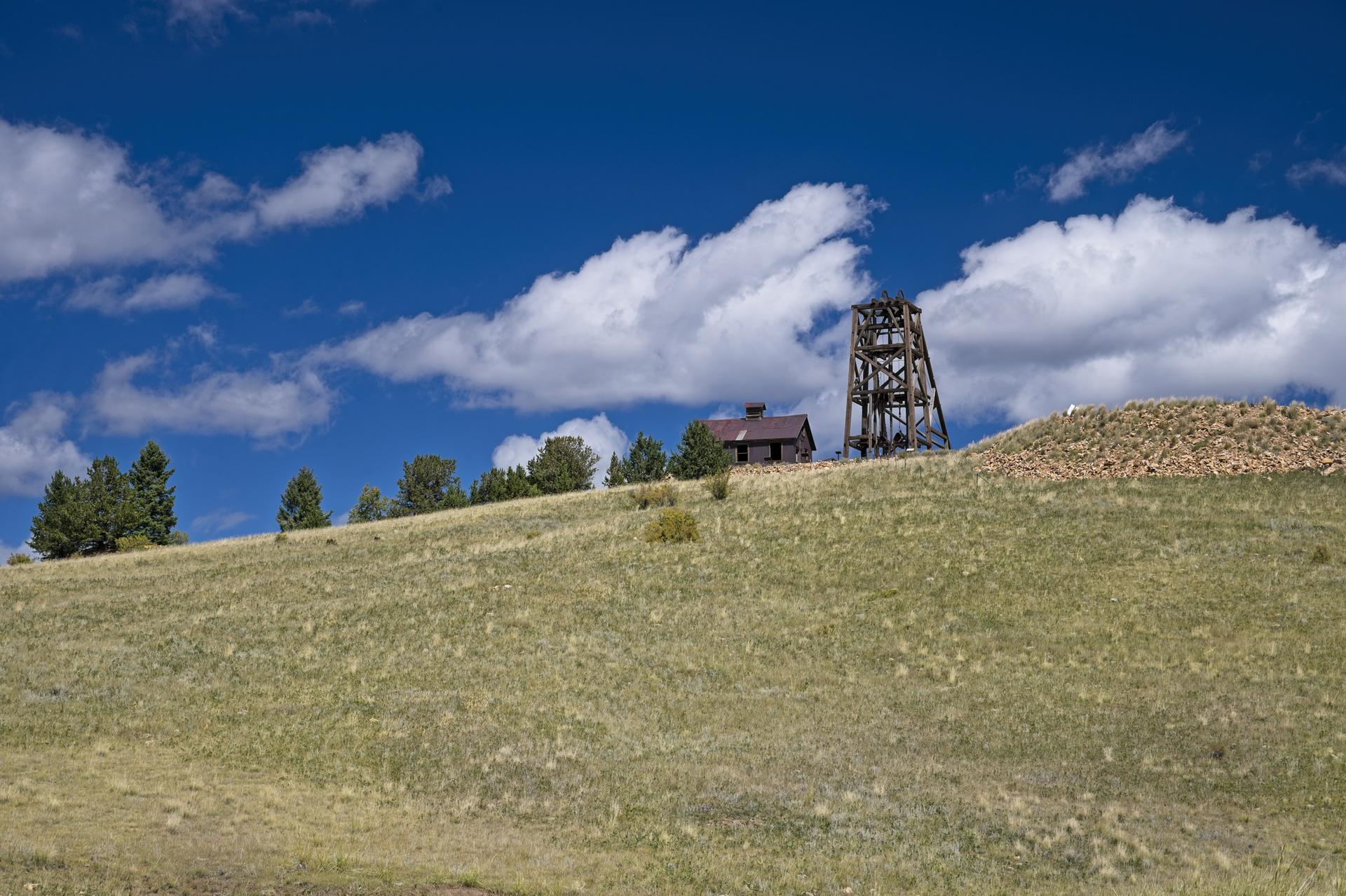 Old mining structures on a grassy hill under a bright, cloudy blue sky.
