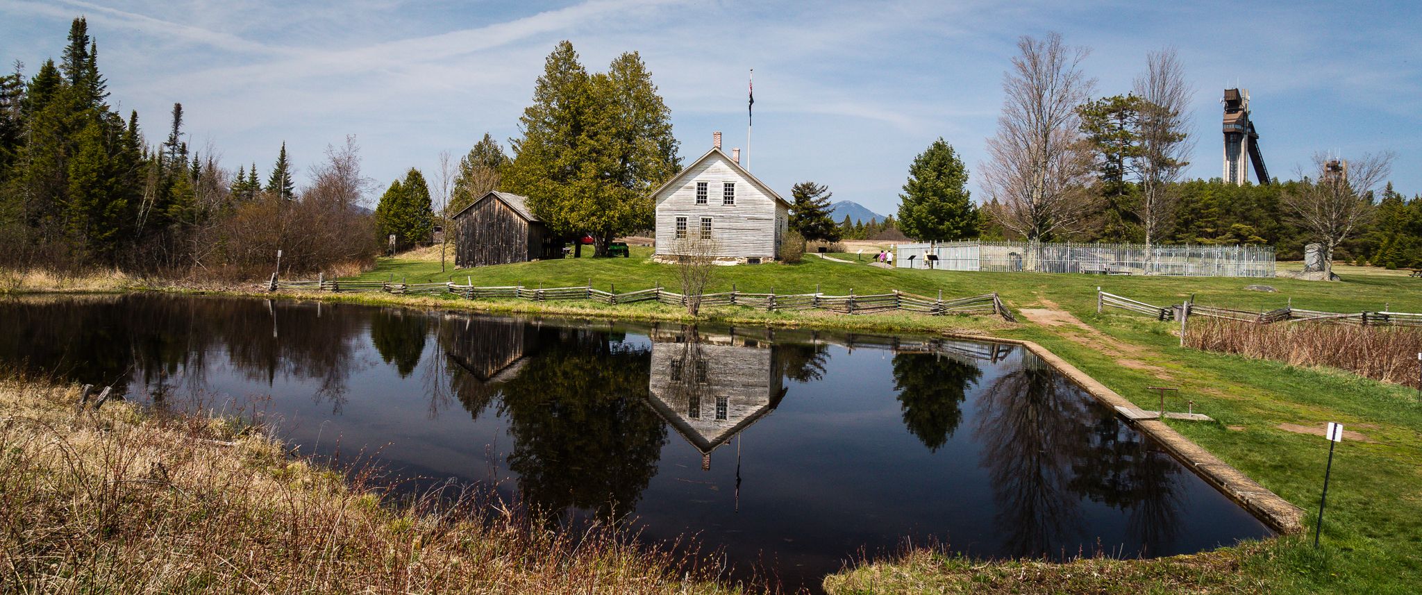 Wooden house and barn reflected in a calm pond under a bright sky. - Heaven Hill Trails loop from Henry's Woods