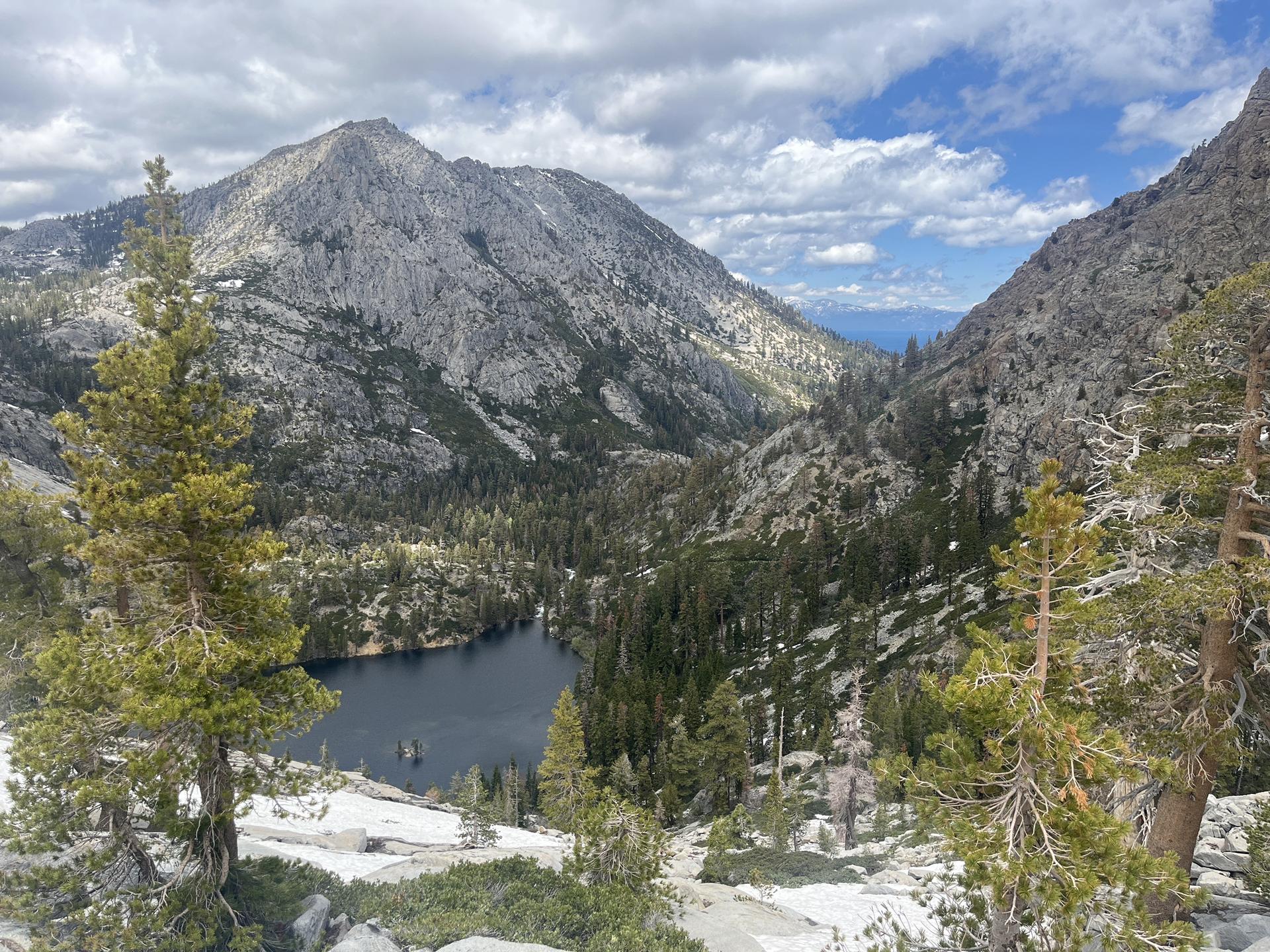 Mountain lake surrounded by rocky peaks and pine trees under a cloudy sky.