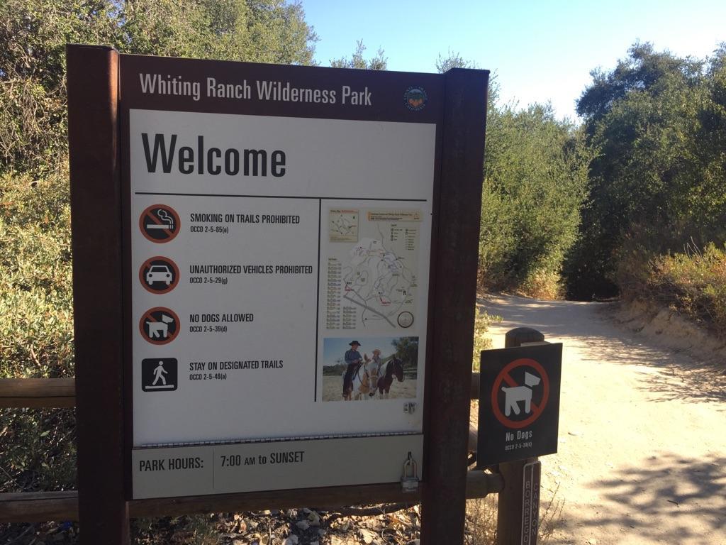 Park welcome sign with rules and map next to a dirt path.