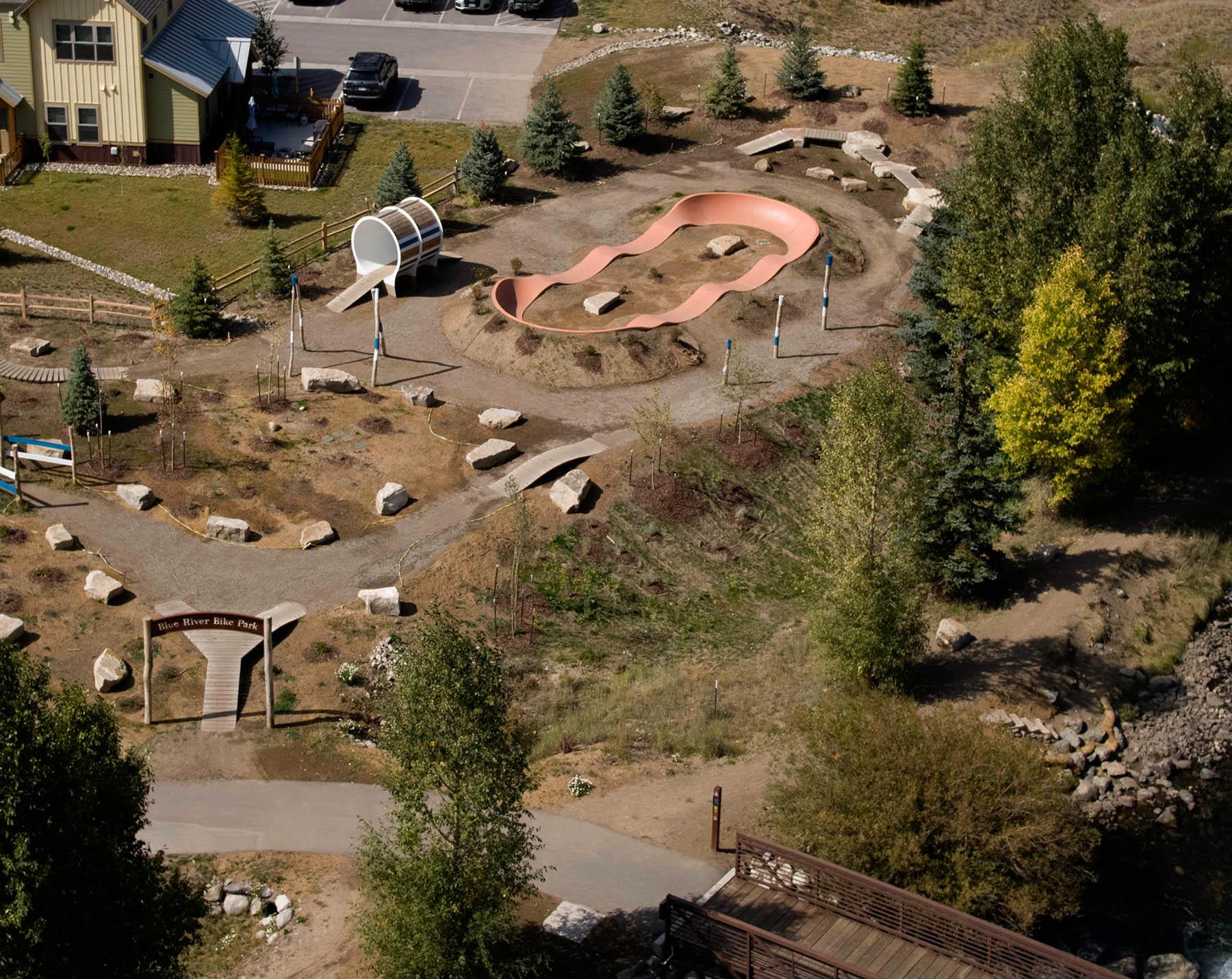 Aerial view of a park with a pump track, paths, and surrounding buildings.