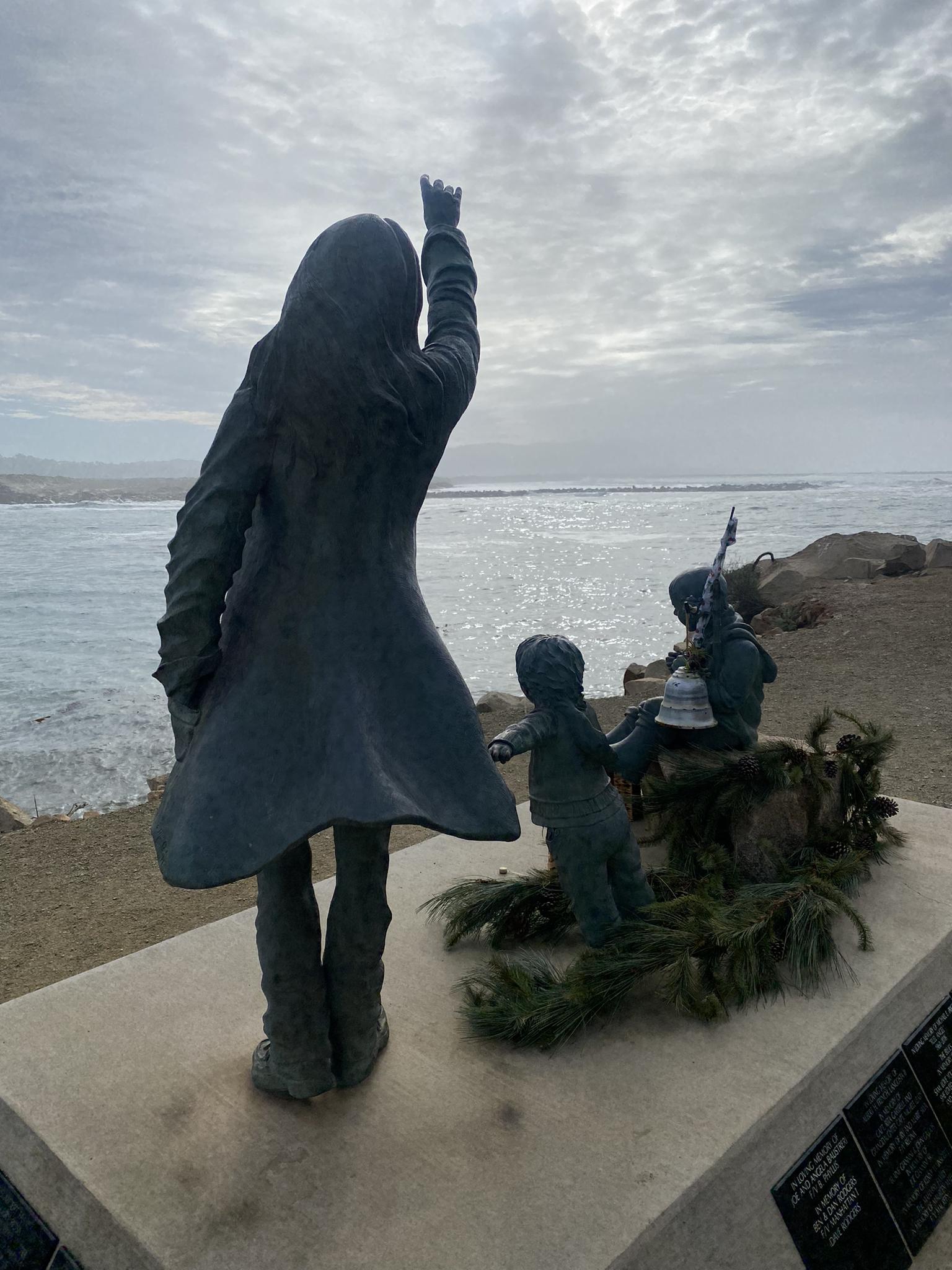 Bronze statues of a woman and children overlooking a cloudy ocean.