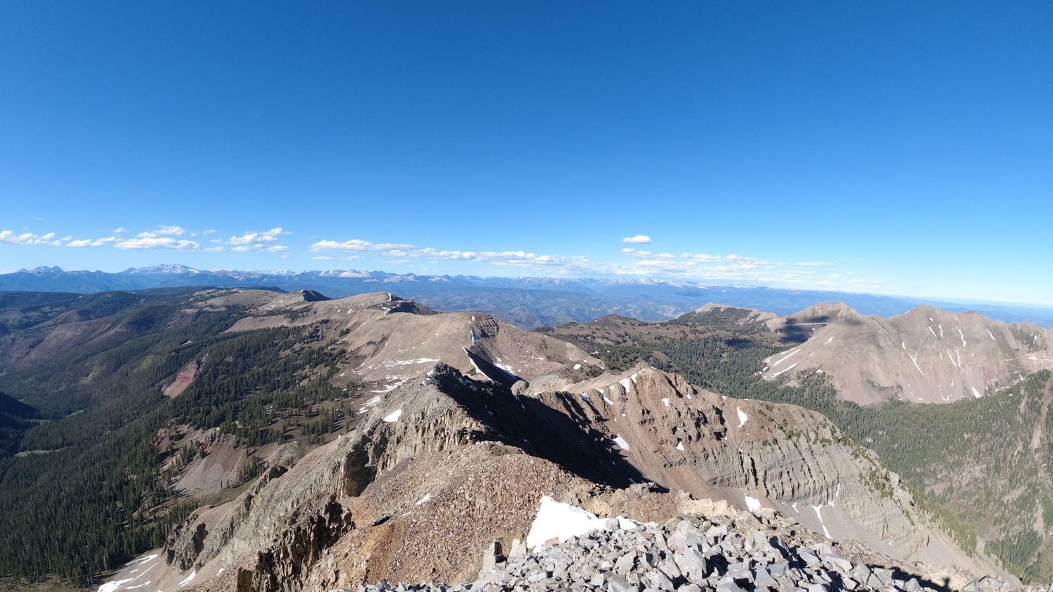 Sunny panoramic view of rocky mountain peaks and forested valleys.