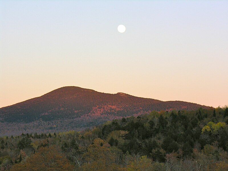 A full moon hangs over forested mountains with autumn colors at dusk. - Mount Chase Trail