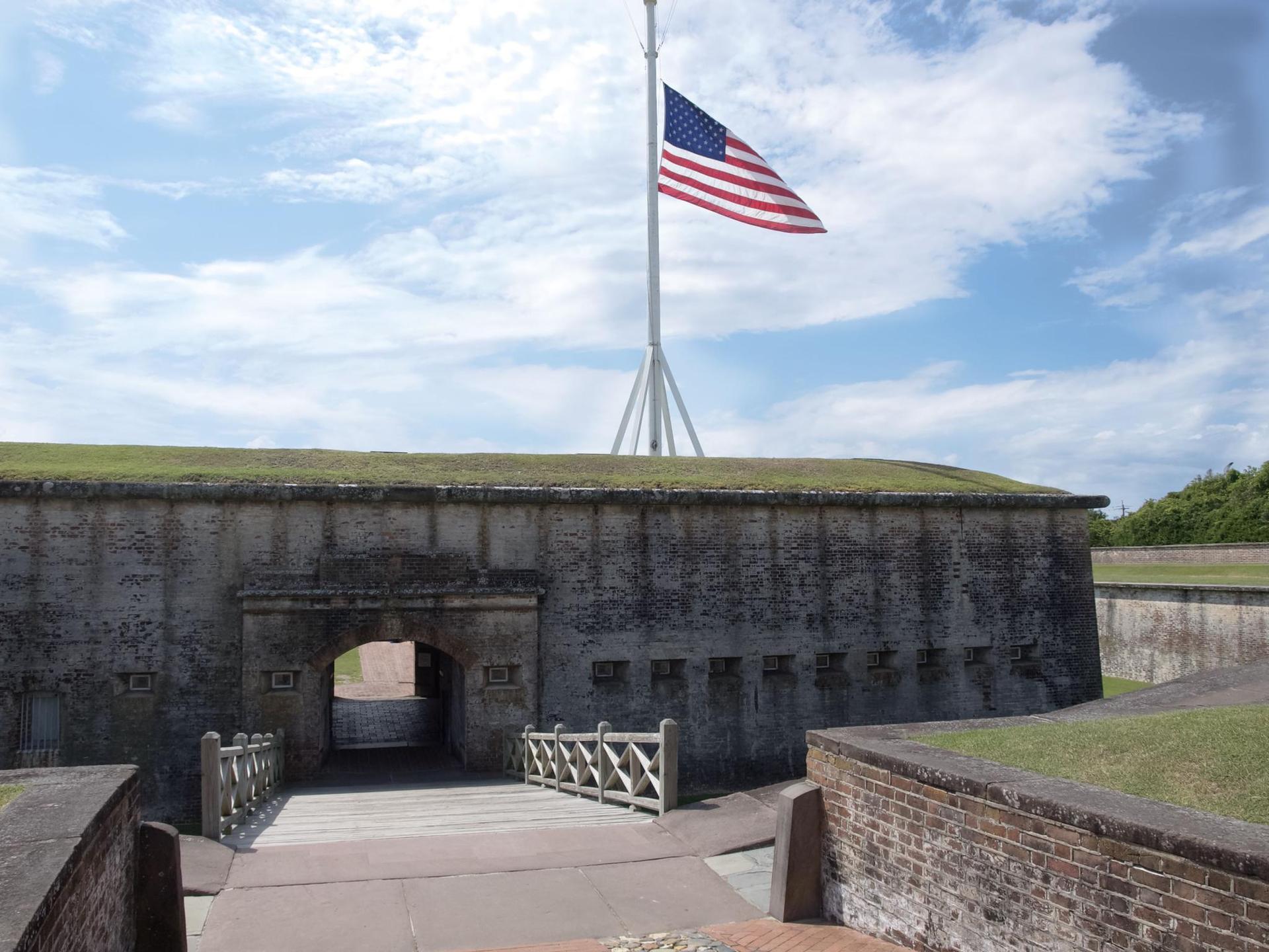 An American flag flies above a historic stone fort entrance on a sunny day.
