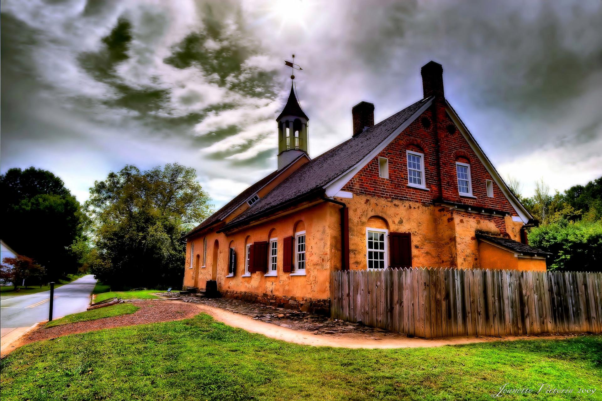 Historic brick building with a steeple, under a dramatic, cloudy sky.