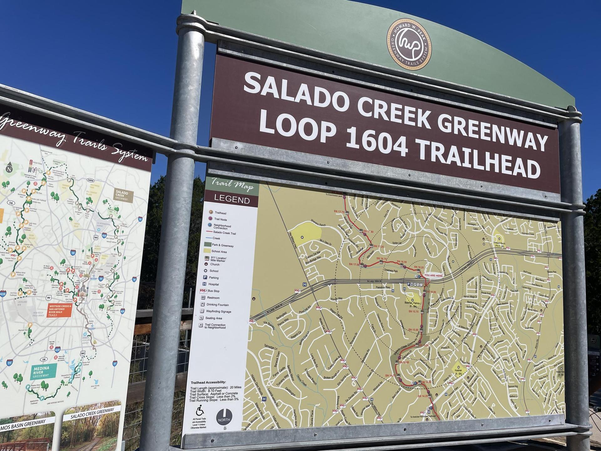 Large outdoor sign displaying trail maps under a bright blue sky.