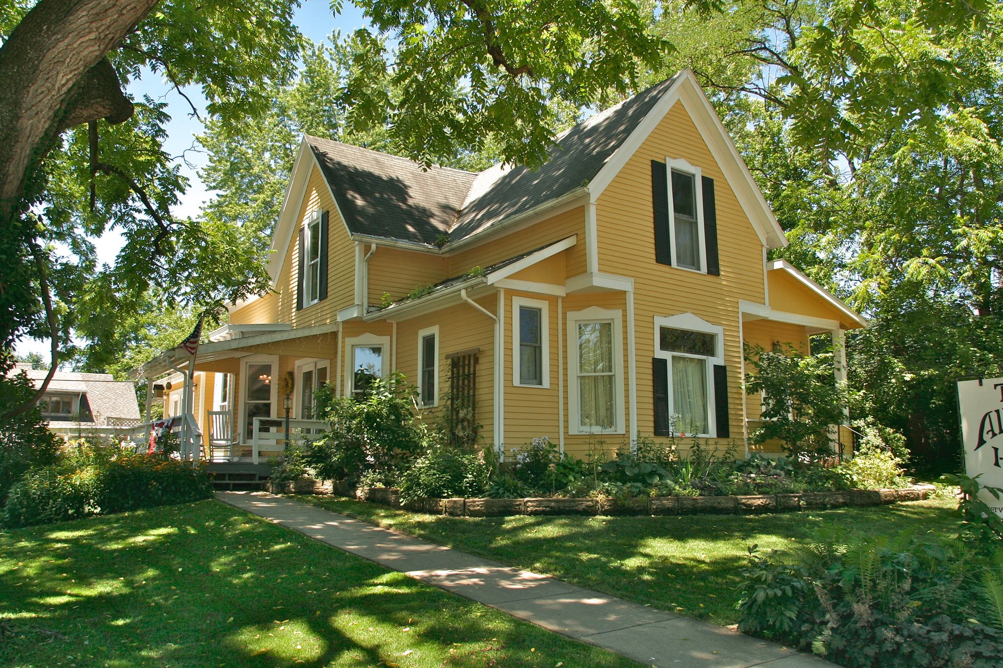 A bright yellow house with black shutters surrounded by lush green trees on a sunny day. - Yellowwood Lake – Nashville, Indiana Town Center loop from Nashville