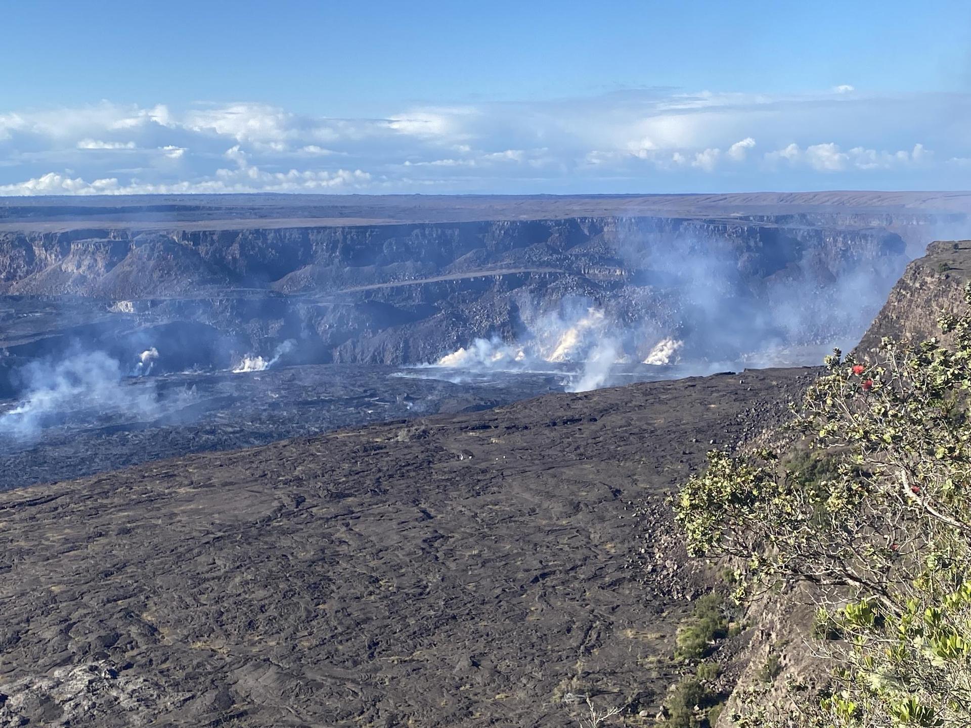 Wide view of a vast, dark volcanic landscape with multiple steam vents.