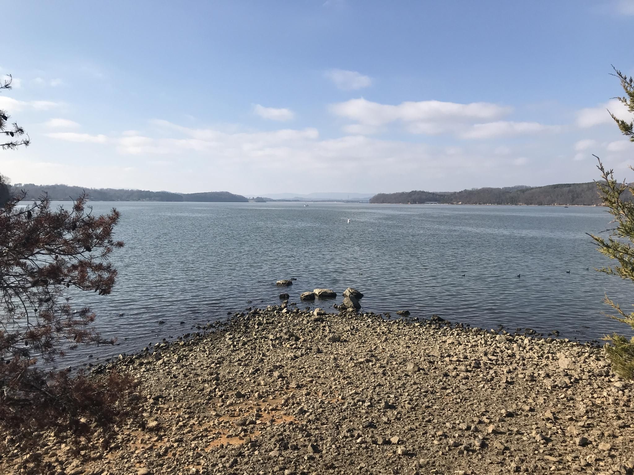 Wide lake with rocky shore under a bright, clear sky. - Outer Loop Trail