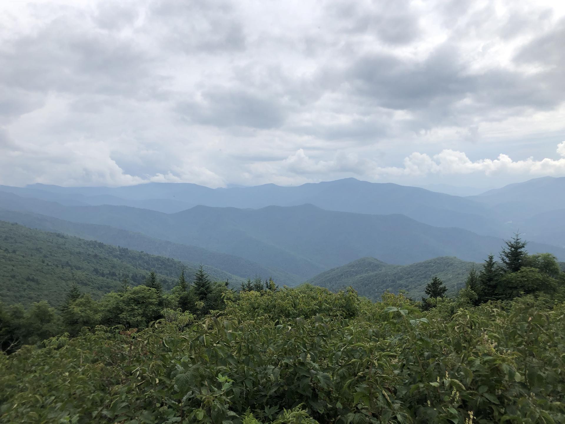 Expansive view of layered green mountains under a cloudy sky.
