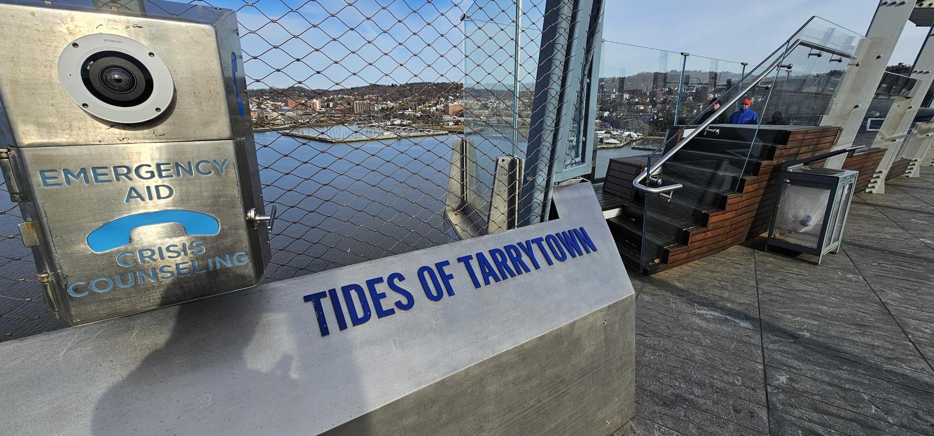 Emergency aid box and sign on a bridge overlooking water and distant town.