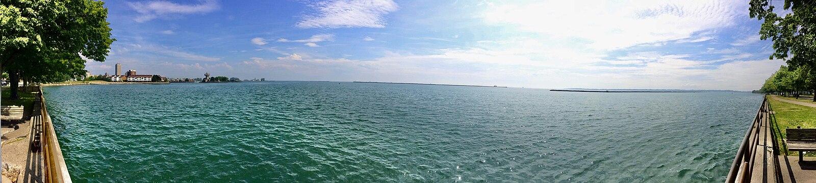 Panoramic view of a vast blue-green lake under a bright, partly cloudy sky.