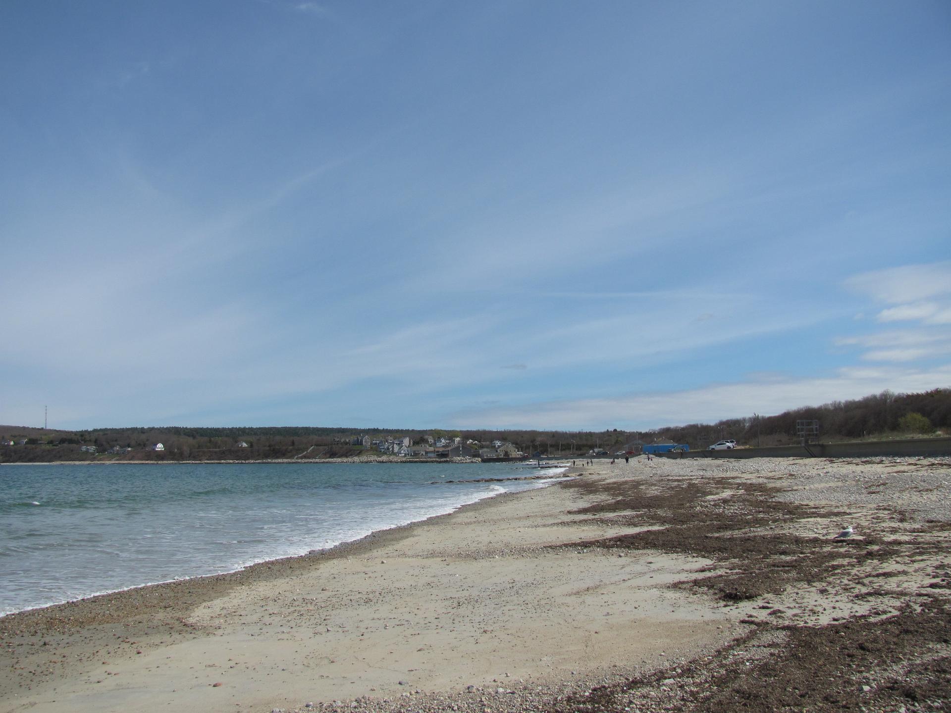 A wide sandy beach with gentle waves and distant figures under a bright sky.