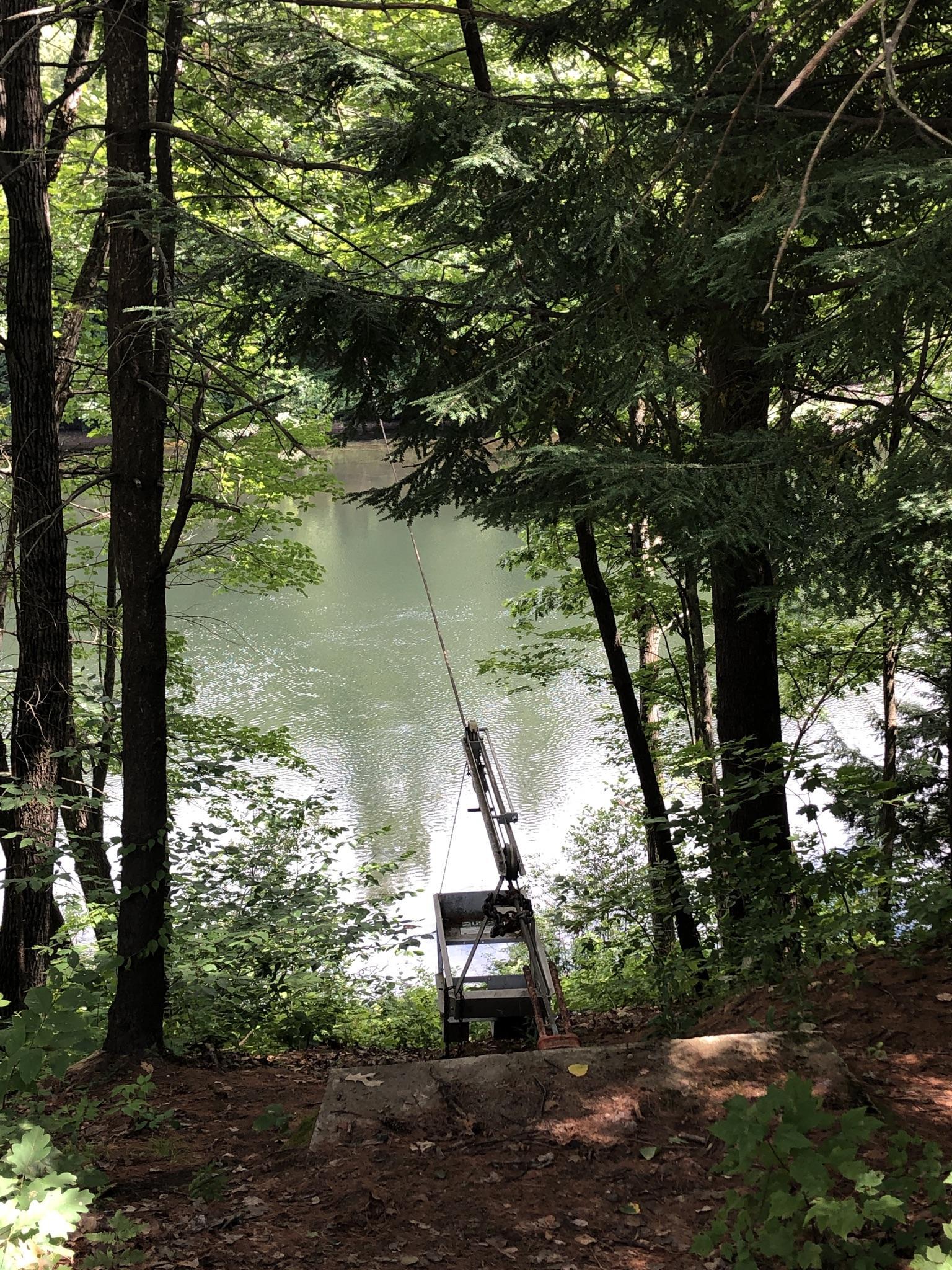 A fishing rod and chair by a river, framed by dense green trees.