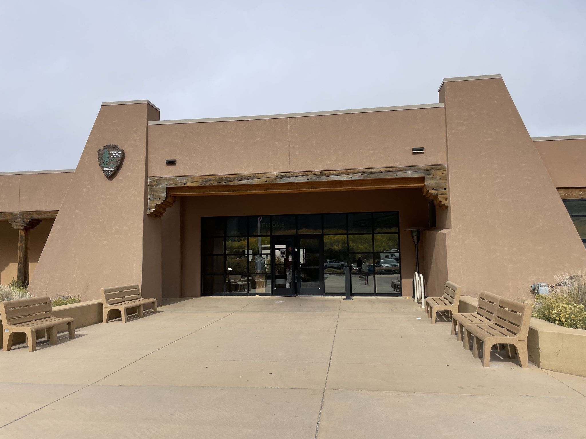 Modern building entrance with large glass doors and outdoor benches under an overcast sky. - Sand Sheet Loop