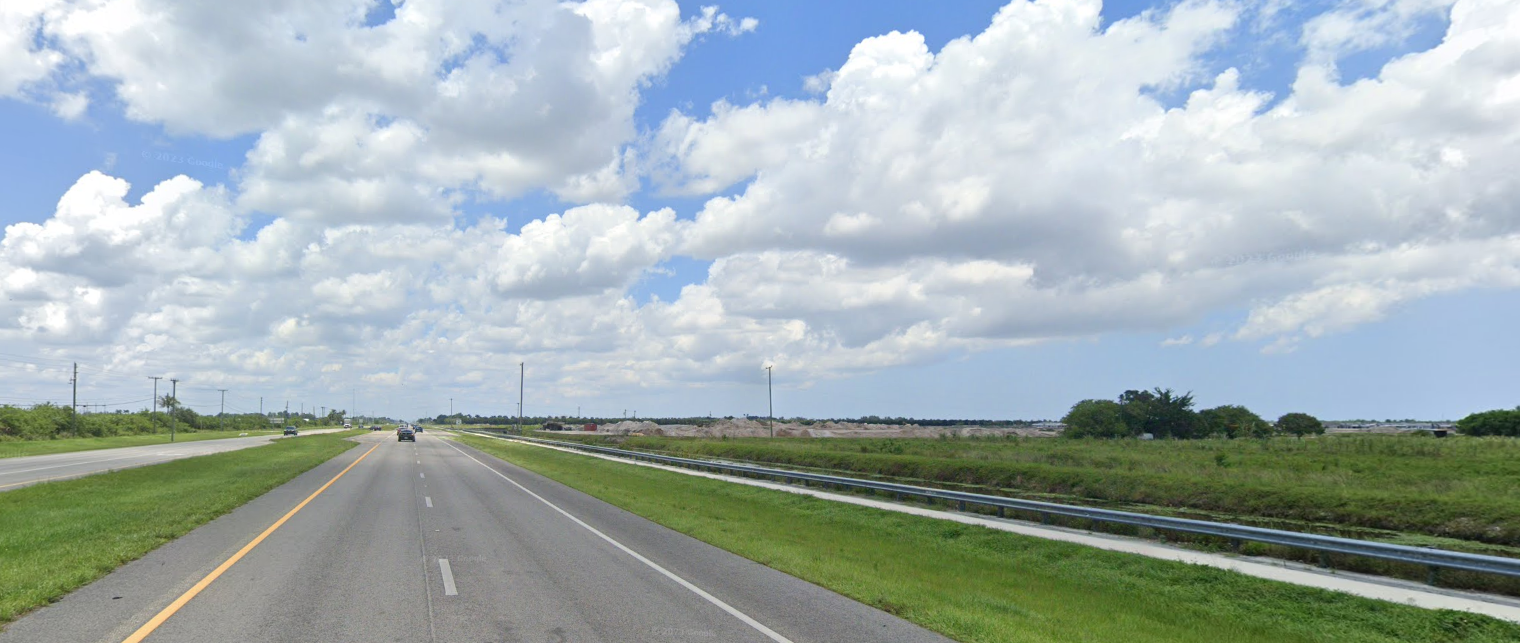Highway with cars driving through a green landscape under a cloudy sky.