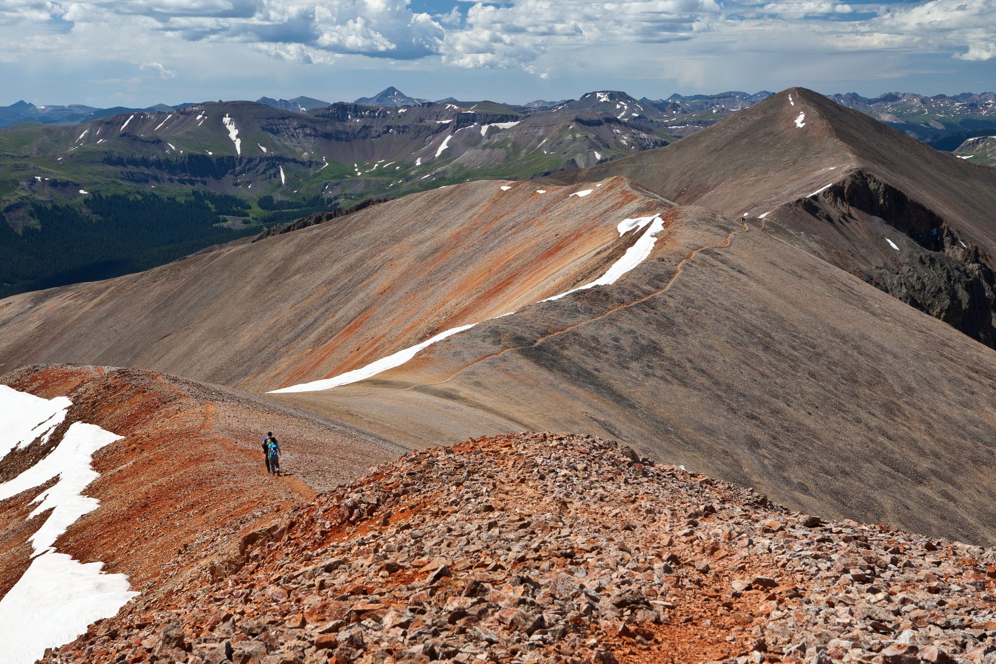 Hiker on a rocky mountain ridge with snow patches under a cloudy sky. - Redcloud & Sunshine Peaks