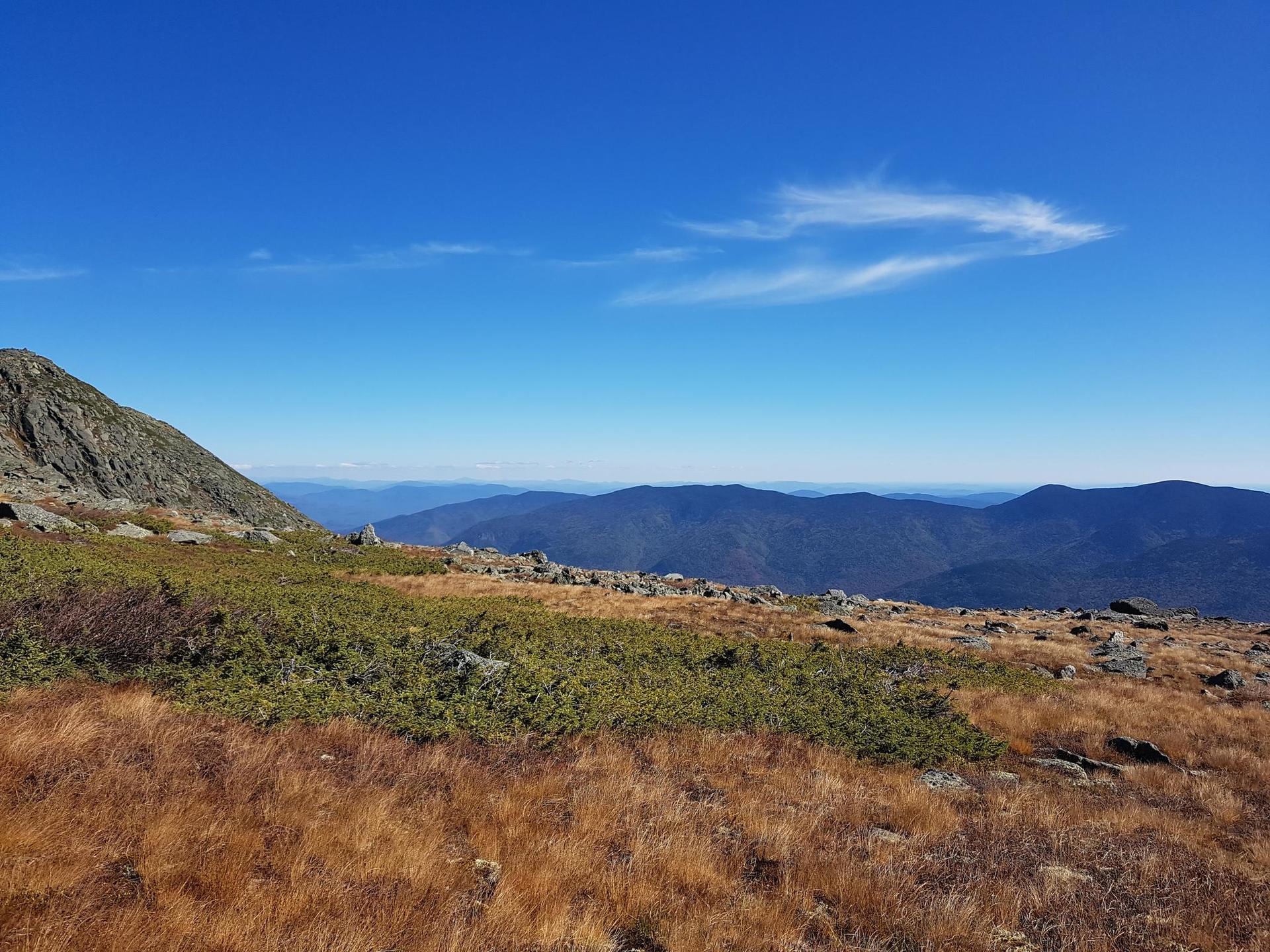 Vast mountain landscape with golden grass and distant peaks under blue sky.