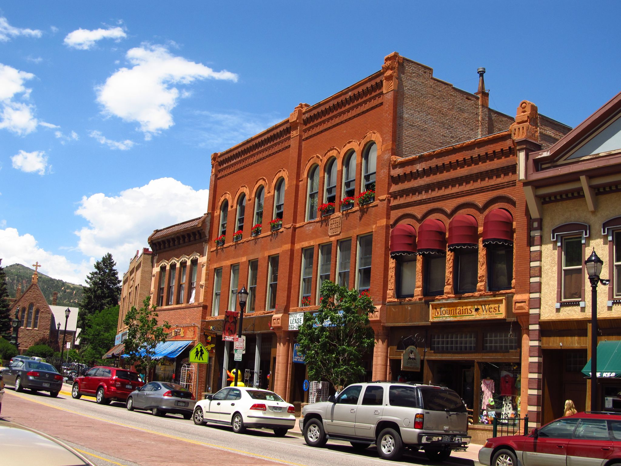 Historic brick buildings line a sunny street with parked cars and blue sky. - Woodland Park via Manitou Springs
