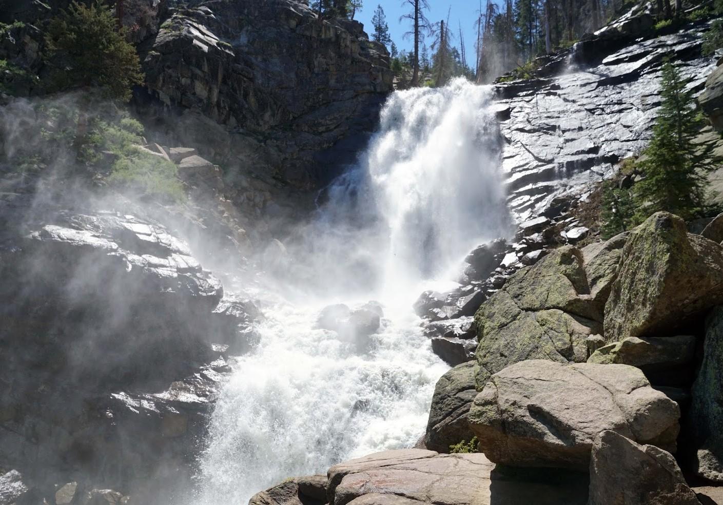 A powerful waterfall cascades down rocky cliffs under a bright sky.