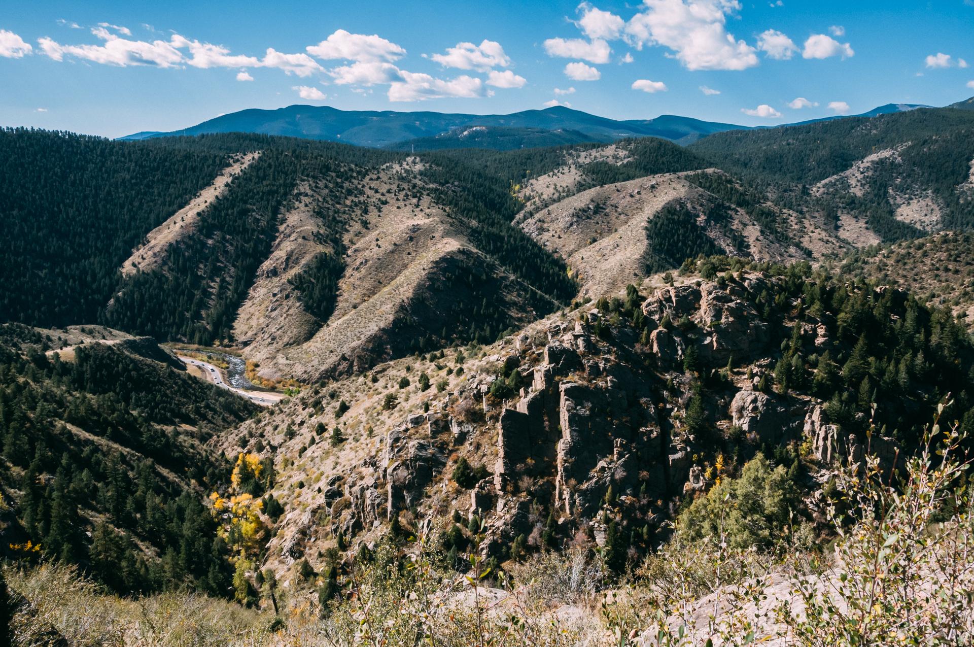 Rugged mountain landscape with deep valleys and forested slopes under a bright sky.