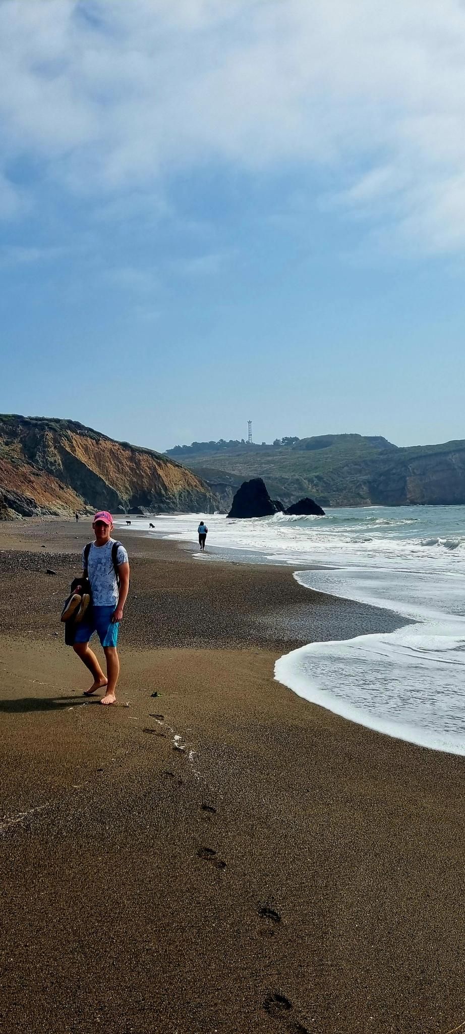 Man with bag walking on a dark sand beach with waves and cliffs. - Coastal, Wolf Ridge, and Miwok Trails Loop