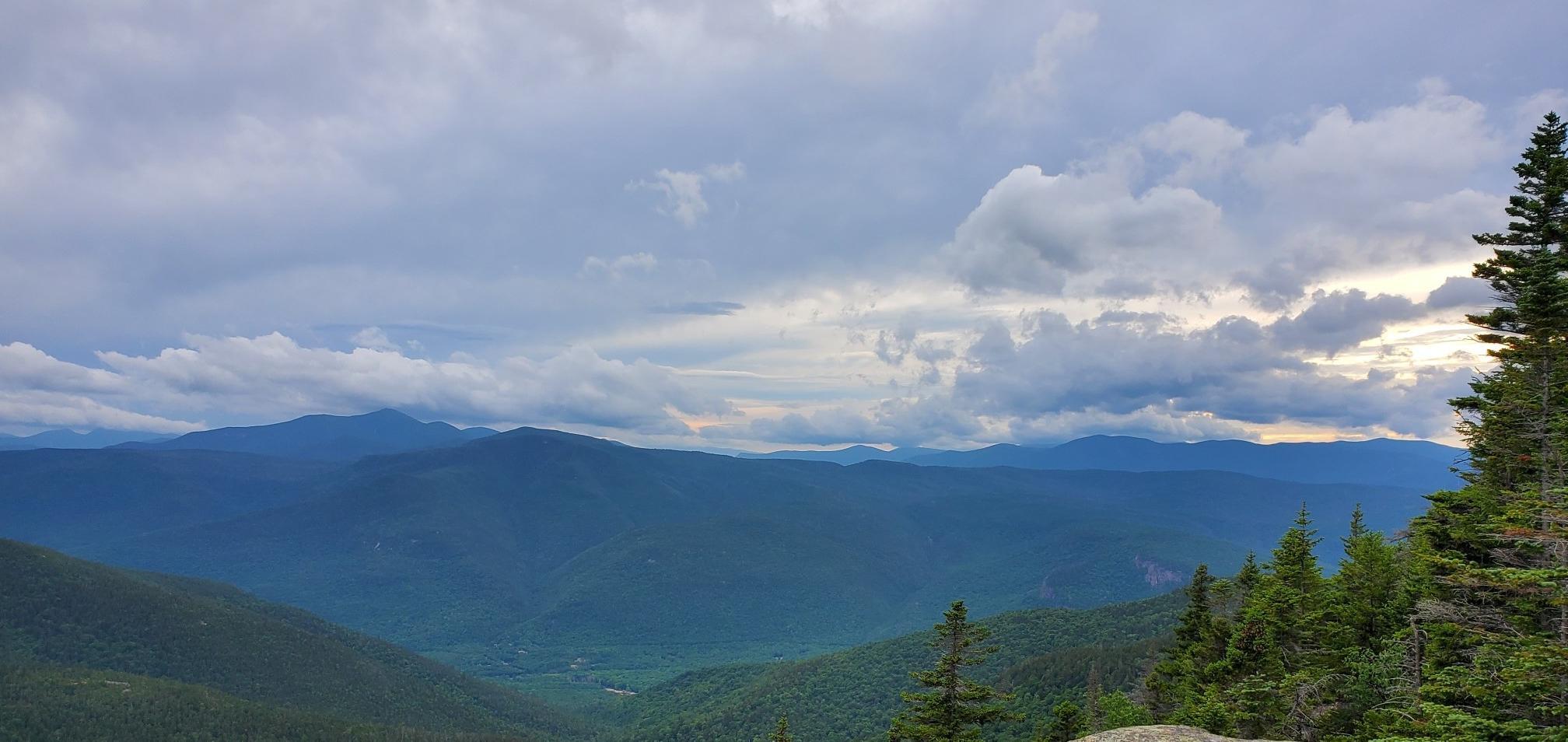 Panoramic view of distant mountains and a forested valley under cloudy skies.