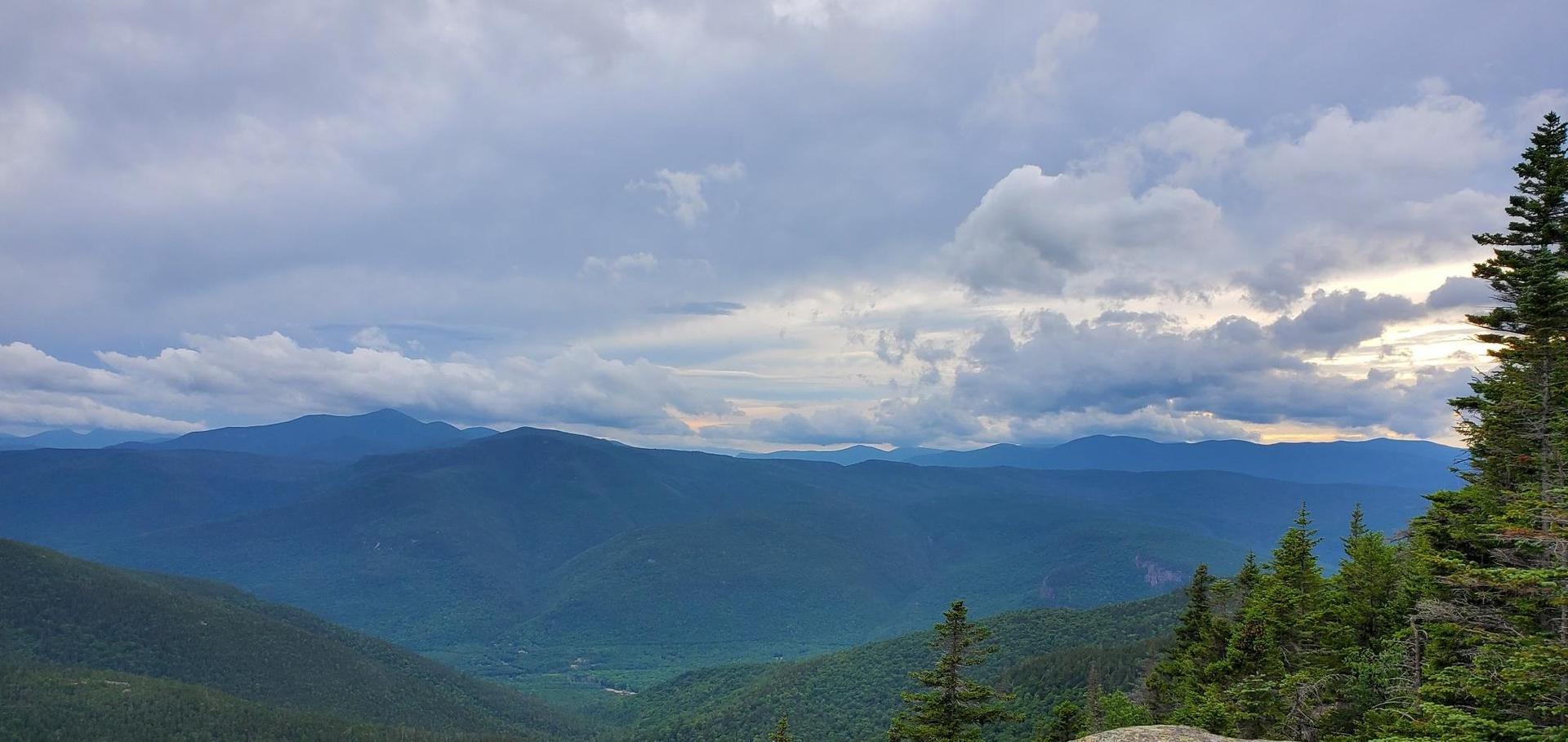 Panoramic view of distant mountains and a forested valley under cloudy skies.