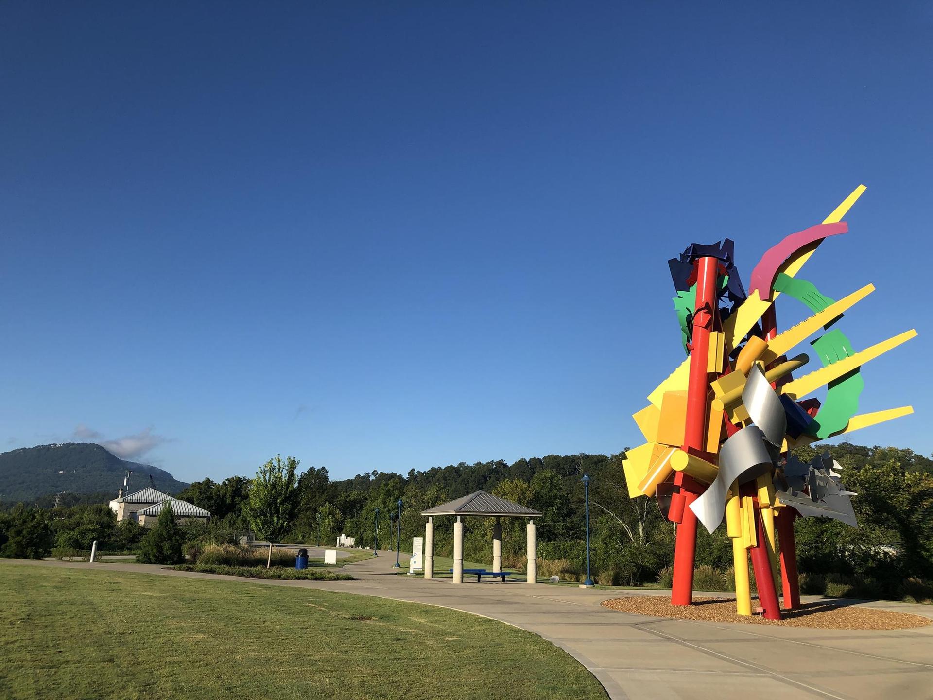 Colorful abstract sculpture in a sunny park with a path and gazebo.