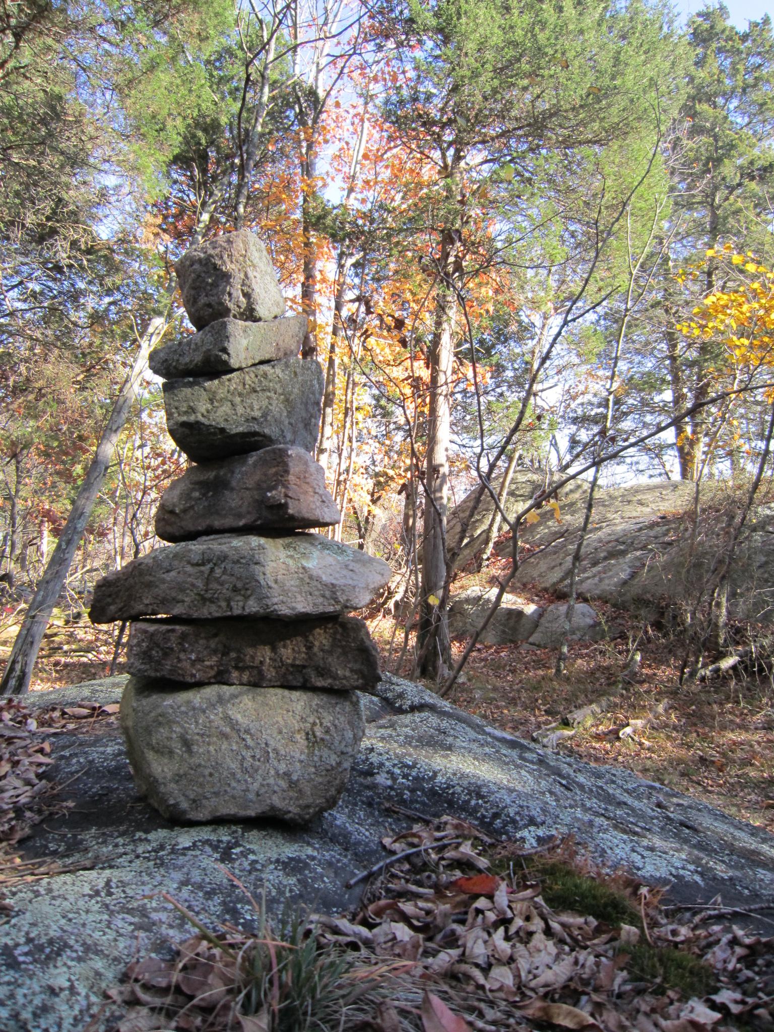 Stacked rock cairn on a rocky forest floor with autumn leaves.